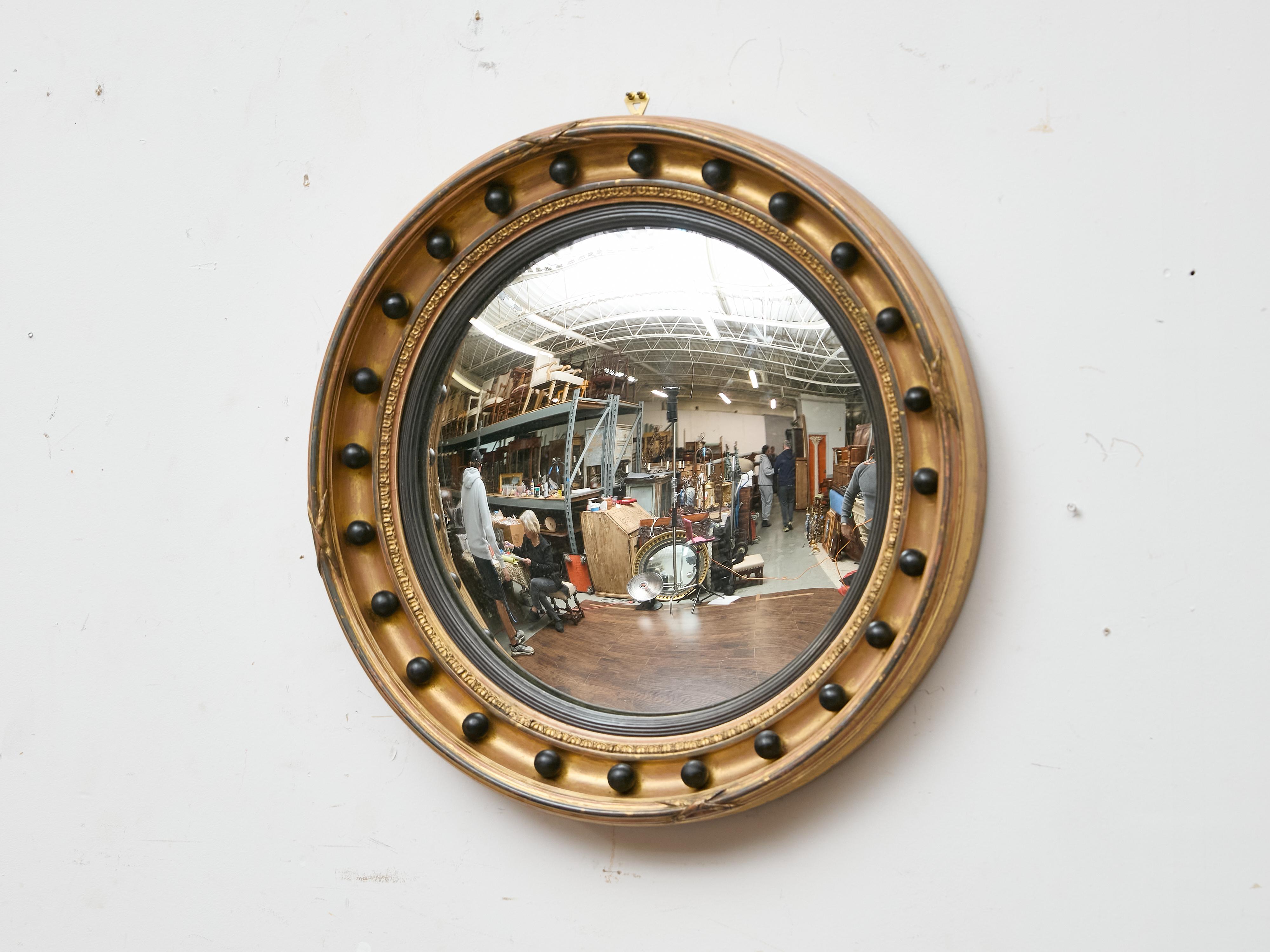 Miroir convexe en bois doré de style Régence anglaise du début du XIXe siècle, remarquable pour sa forme circulaire classique et ses détails décoratifs audacieux. Le cadre mouluré est orné d'une barbotine intérieure sculptée continue et d'une bande