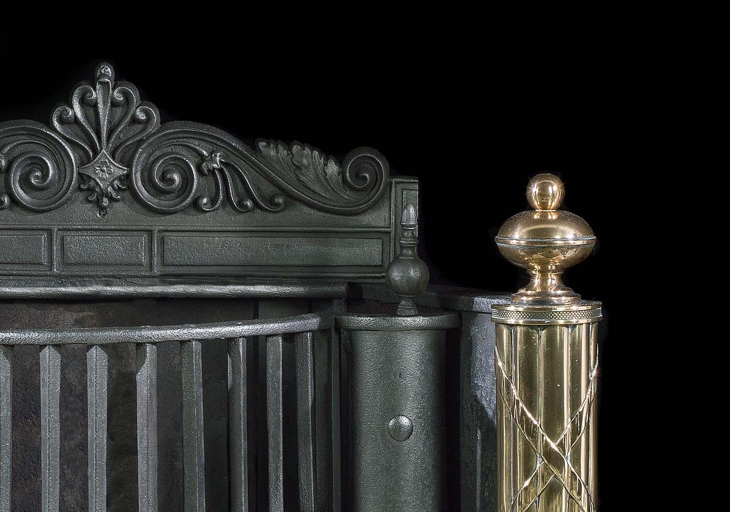 A large and impressive English Regency iron, steel and polished brass antique fire basket with a decorative stele crest backplate. The deep bow fronted grate, above a cut and linked medallion skirt, is supported by a pair of large brass standards