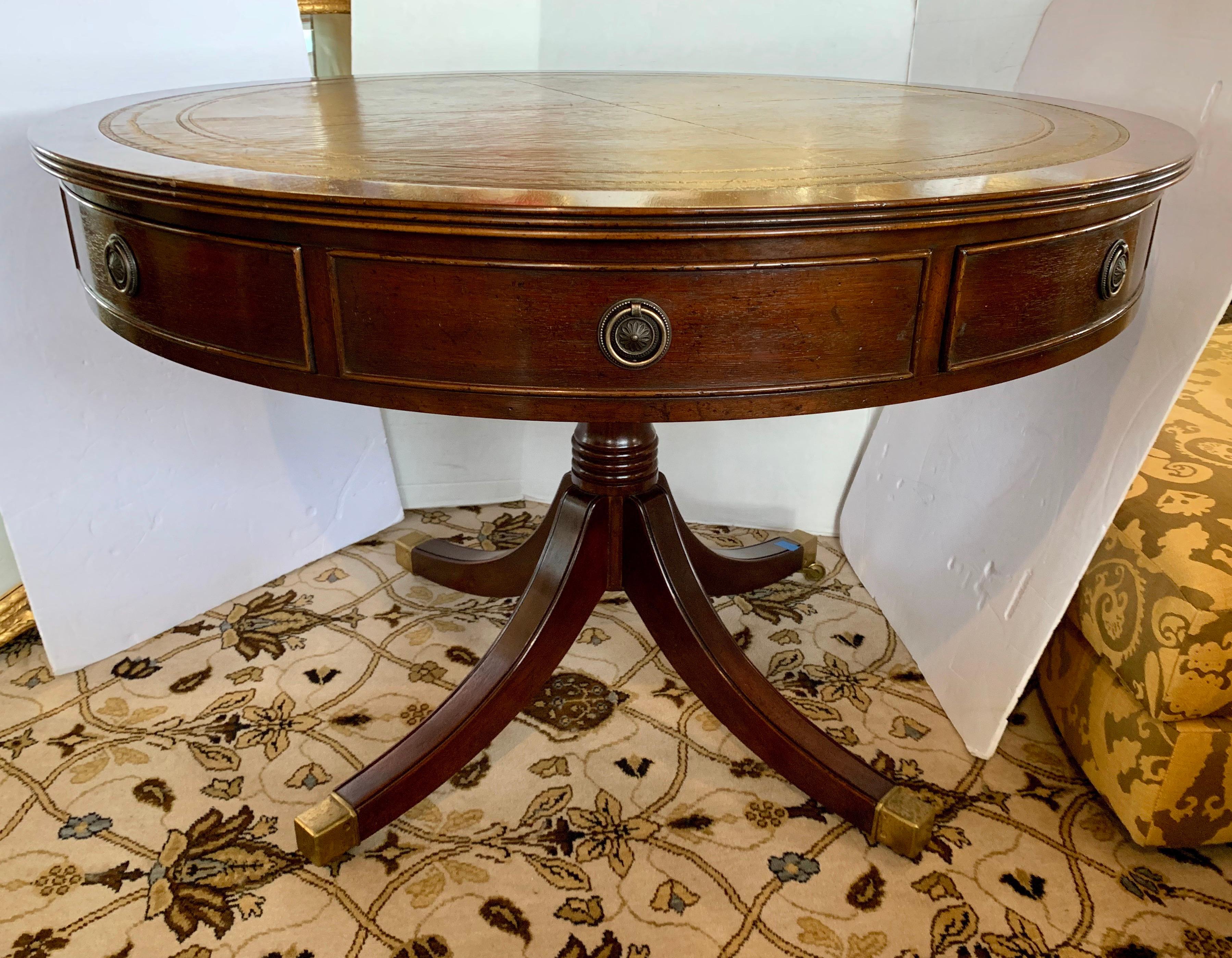 This large handsome George III leather top mahogany drum-table has a tooled leather insert top and includes four drawers and four dummy drawers with original brass handles. The table sits on a baluster pedestal base with brass capped casters. Use as