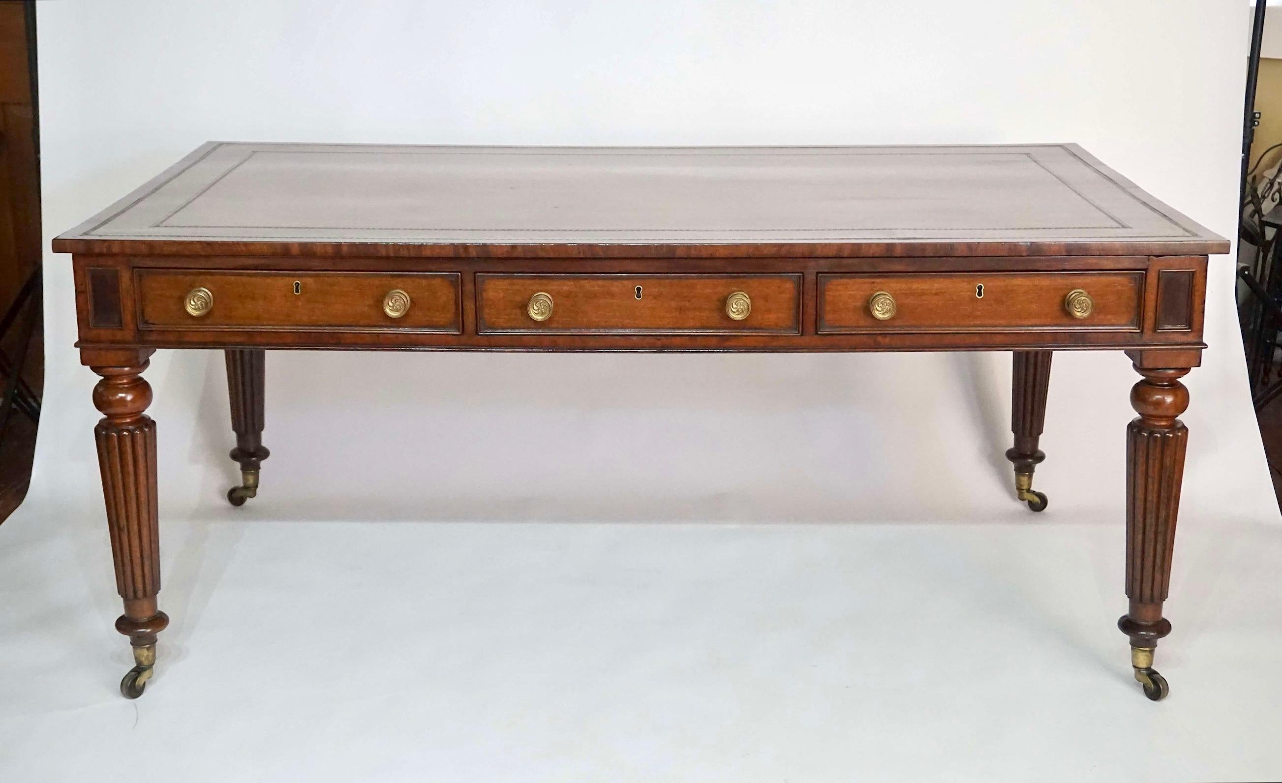 A fine circa 1820 English Regency period double-sided library or writing table of large rectangular form, the gilt-tooled brown leather inset top with square edge above bookended corners with rectangular ogee molded burled wood reserves, long aprons