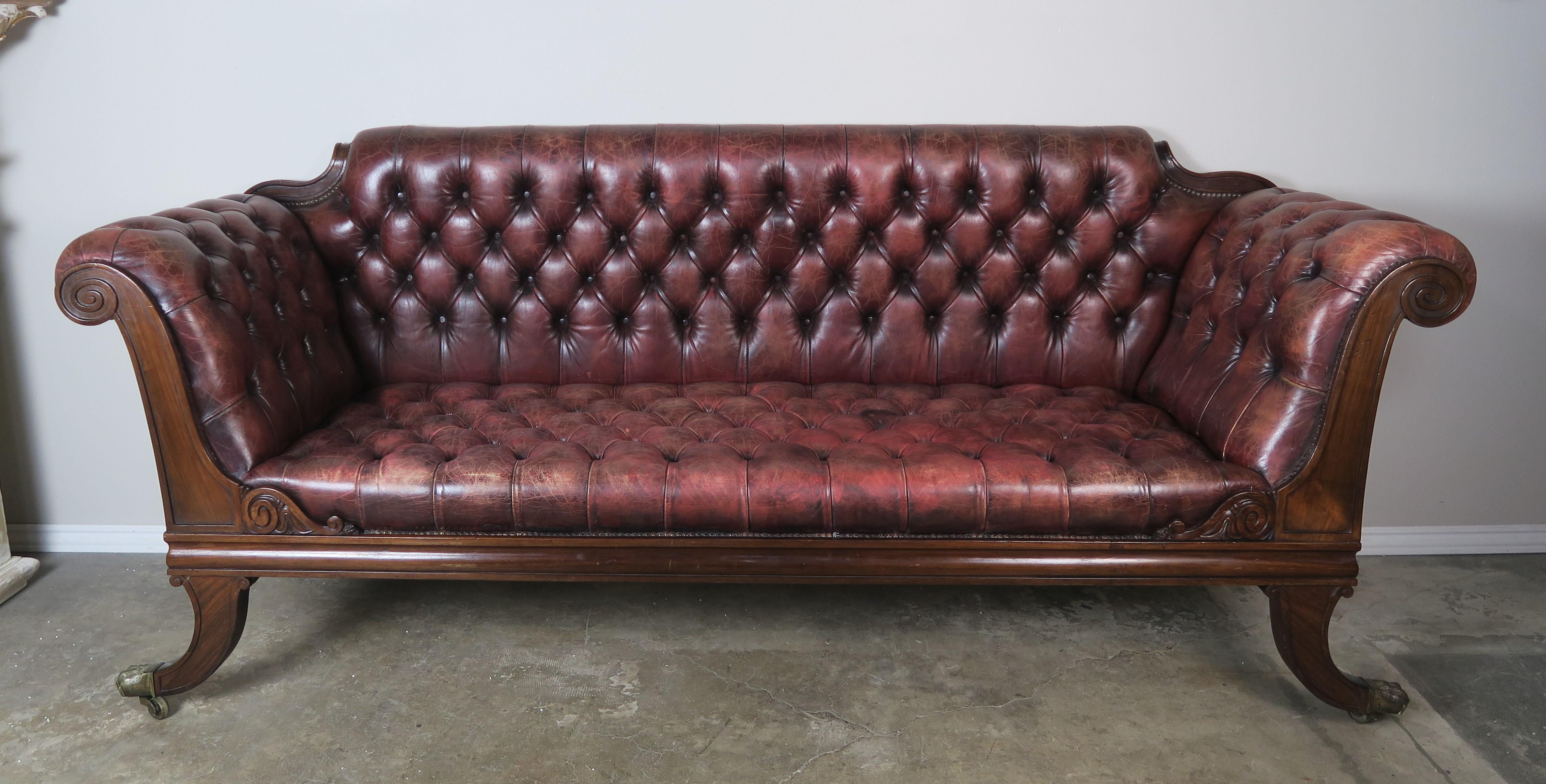 English Regency style leather tufted sofa standing on four curved legs with brass paw feet. Original tufted leather in a beautiful shade of auburn. Antique brass colored nailhead trim detail. 
Measure: Seat height 19