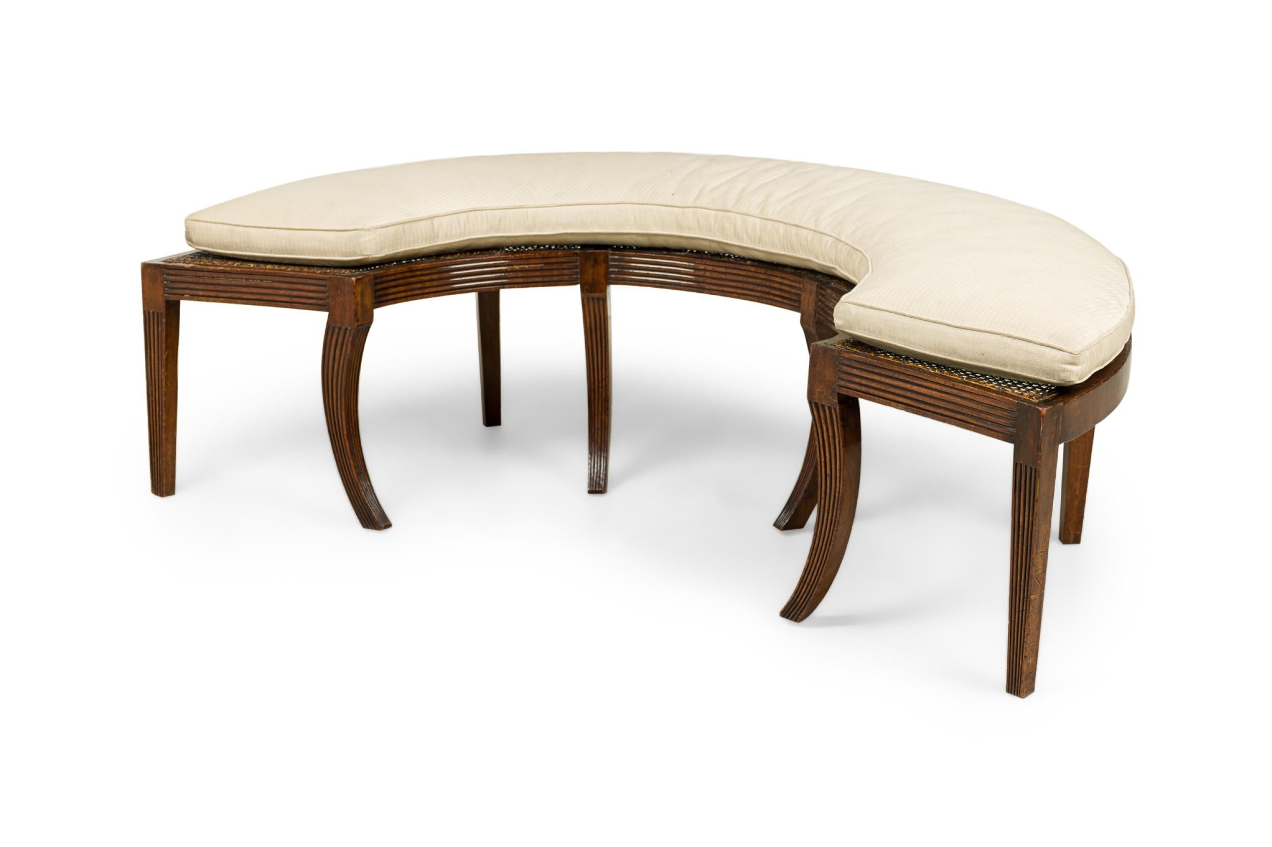 English Regency semi-circular bench with a mahogany frame and caned top, supporting a taupe / brown fabric upholstered seat cushion, resting on 5 square and 4 sabre mahogany legs.
