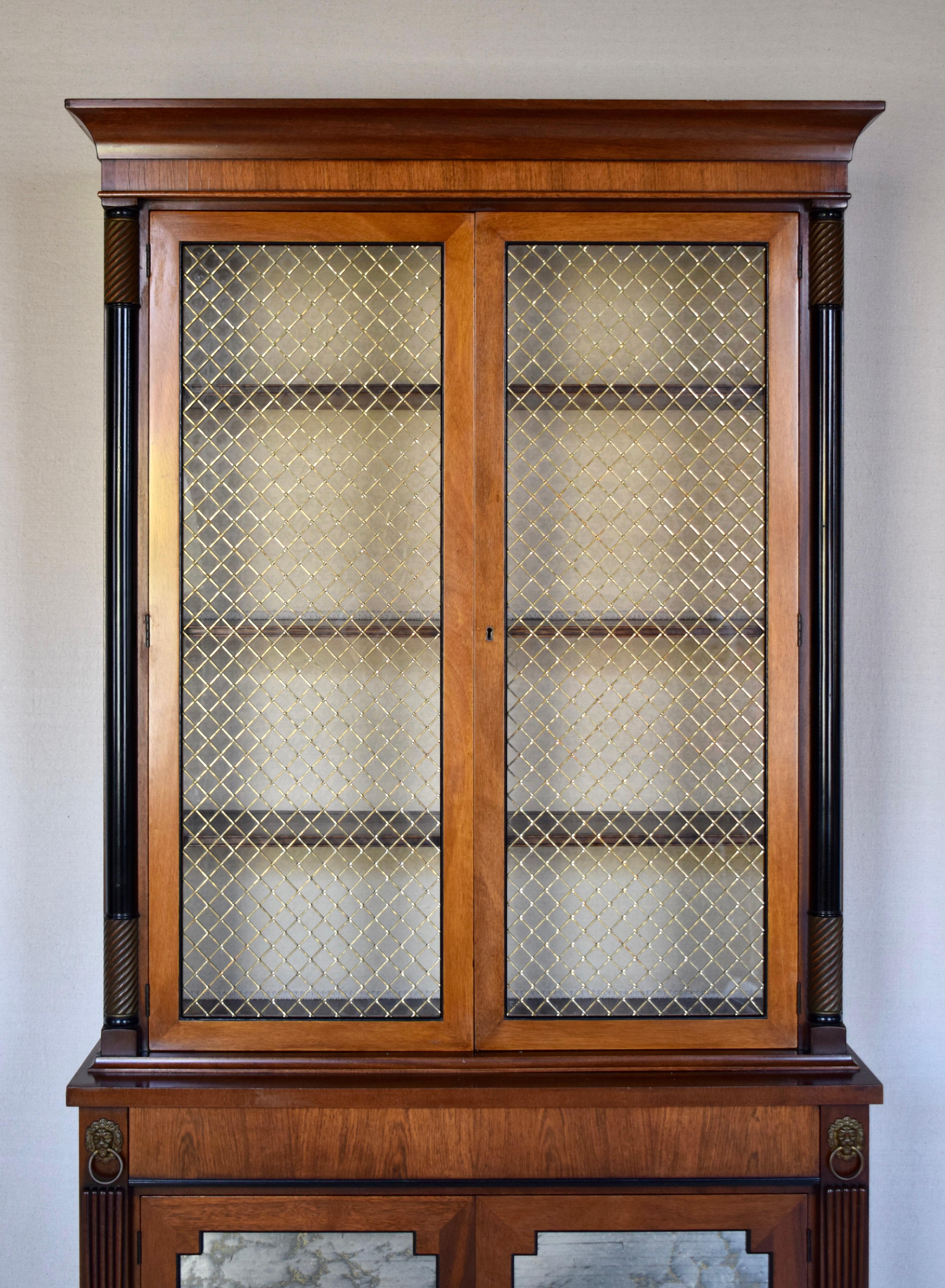 A fine Regency 20th c. banded Mahogany two part bookcase cabinet. Features to the top include the handsome cornice, stately decorative brass & glass grille panel doors flanked by classic spiral turned columns with three adjustable shelves. The