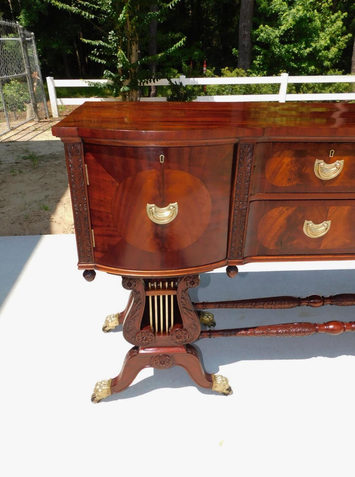 English Regency Mahogany bow front inlaid sideboard with flanking hinged cabinets, three central graduated drawers, flanking carved foliage stiles with acorn finials, original engraved brasses. flanking lyre's with brass tubing, original  mirrors