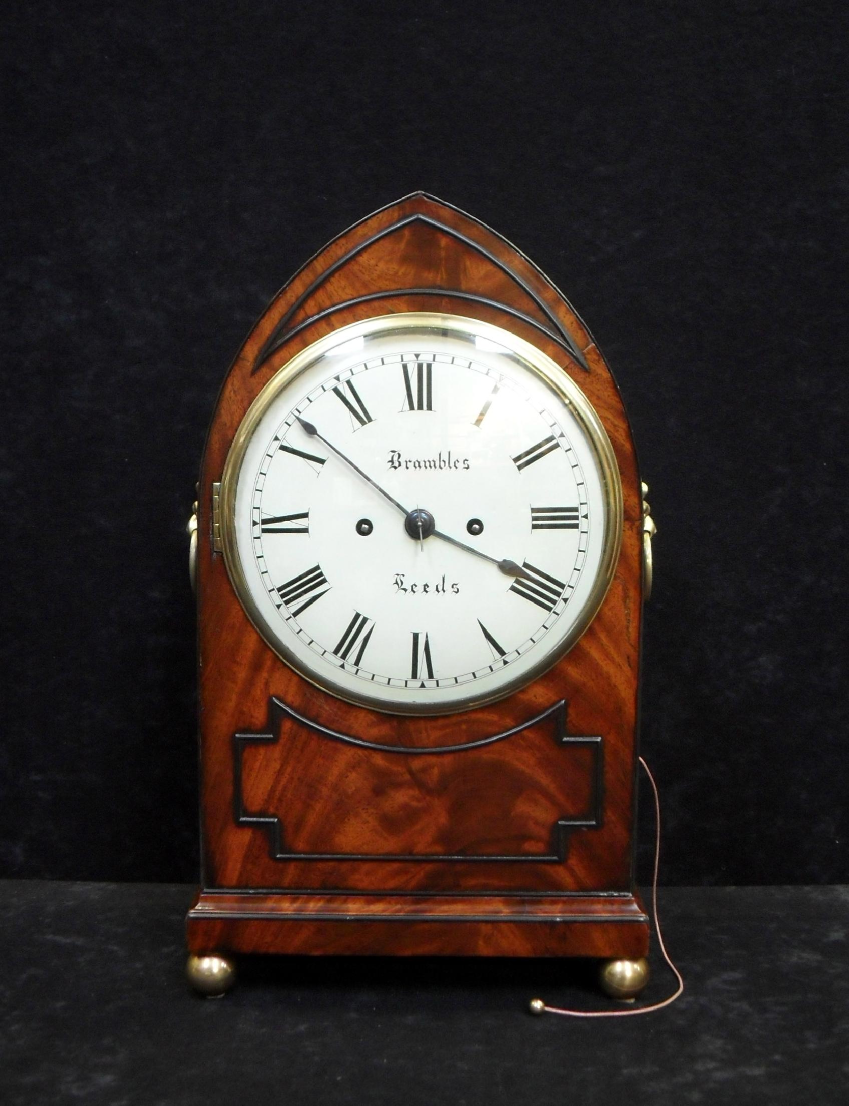 A very good quality figured mahogany lancet top bracket or table clock with ebony raised cockbeaded mouldings to the front on brass ball feet with decorative brass ring carrying handles and side sound frets.
 
The clock has a painted eight inch