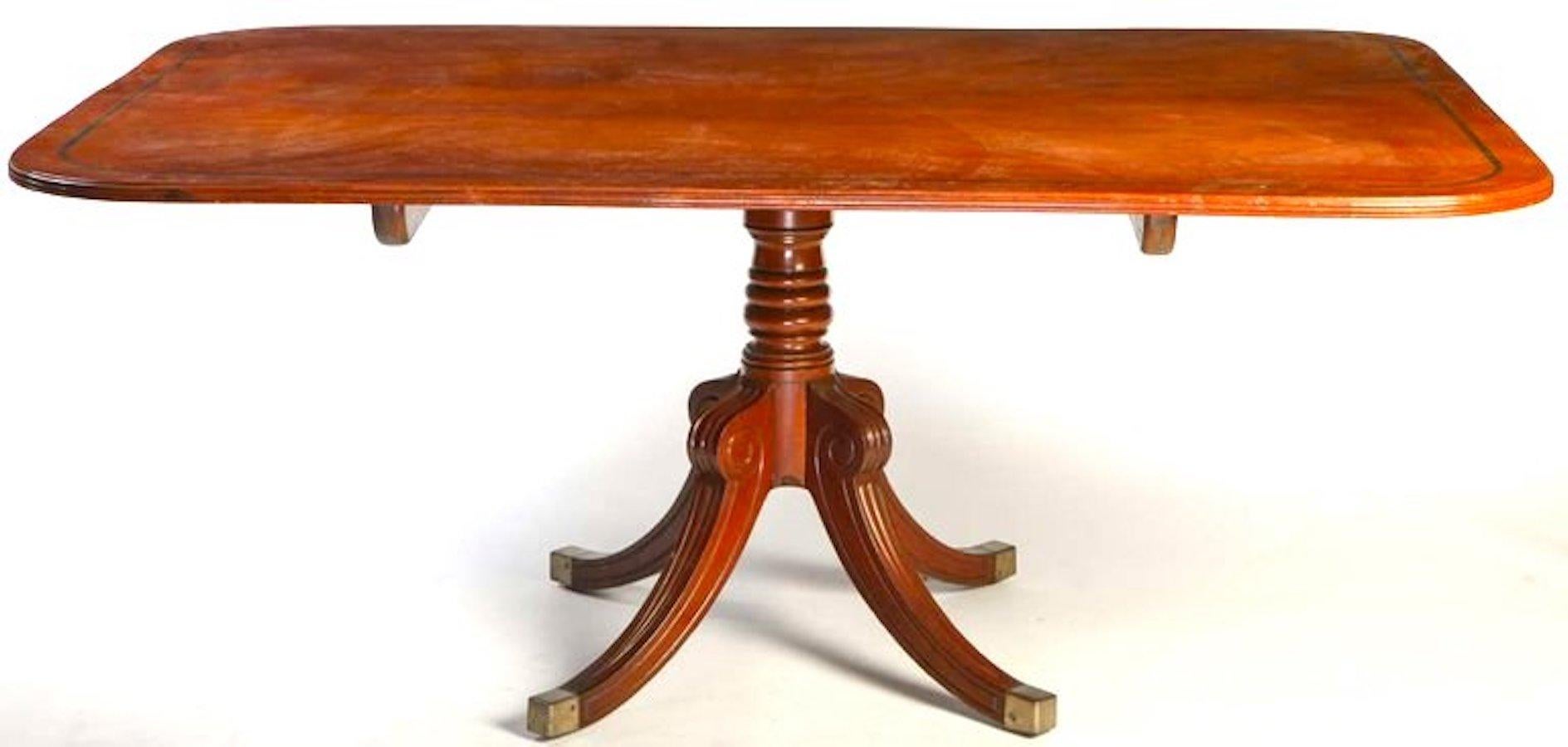 A Regency mahogany breakfast-table with rounded rectangular 
crossbanded tilt-top above a ringturned spreading column and a quadripartite base , brass caps .
 cm.180 x 125 x 76.