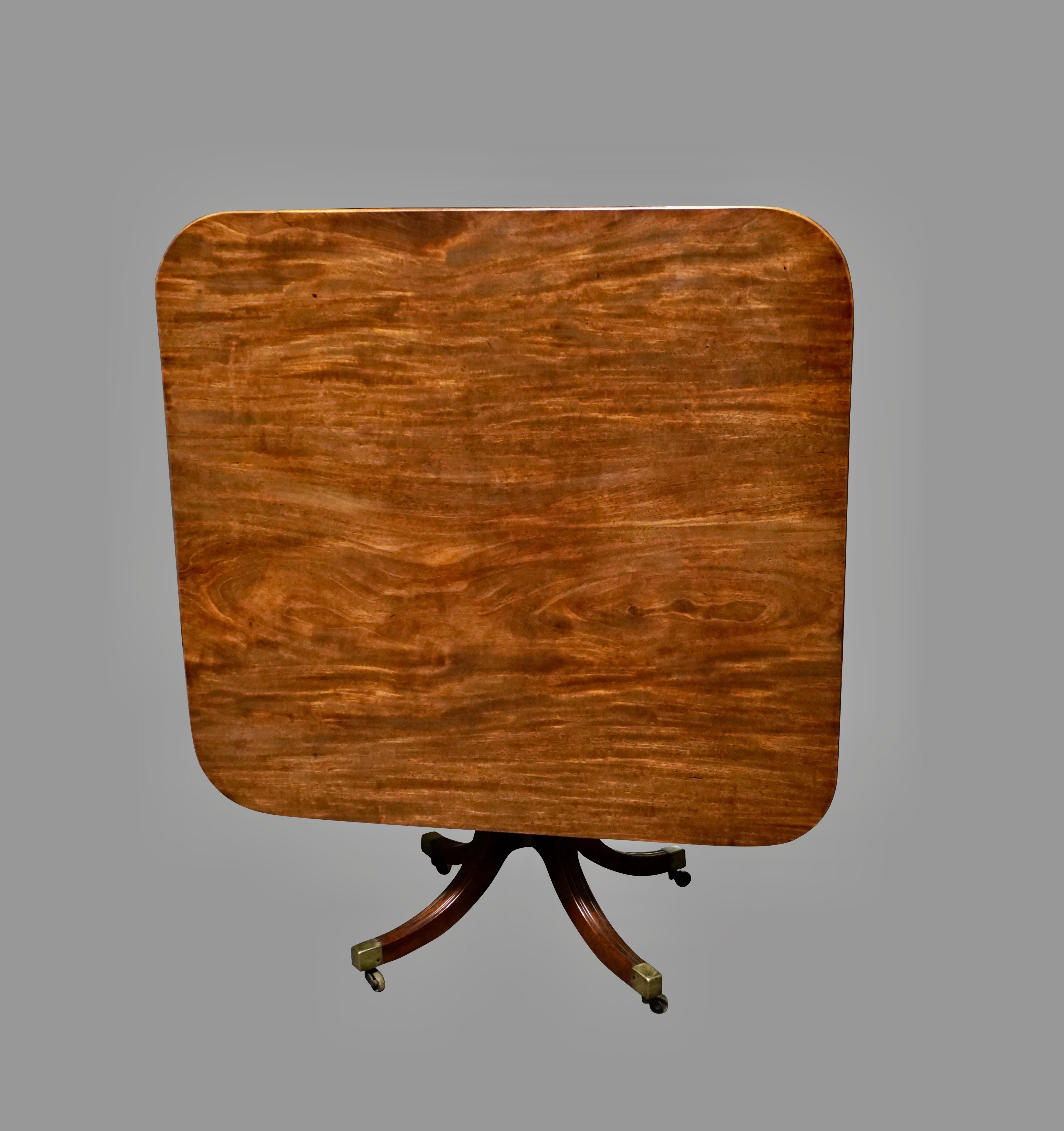 An English figured mahogany breakfast table, the almost square tilt-top with a reeded edge, supported on a reeded downswept quadripartite base ending in brass casters, circa 1815.