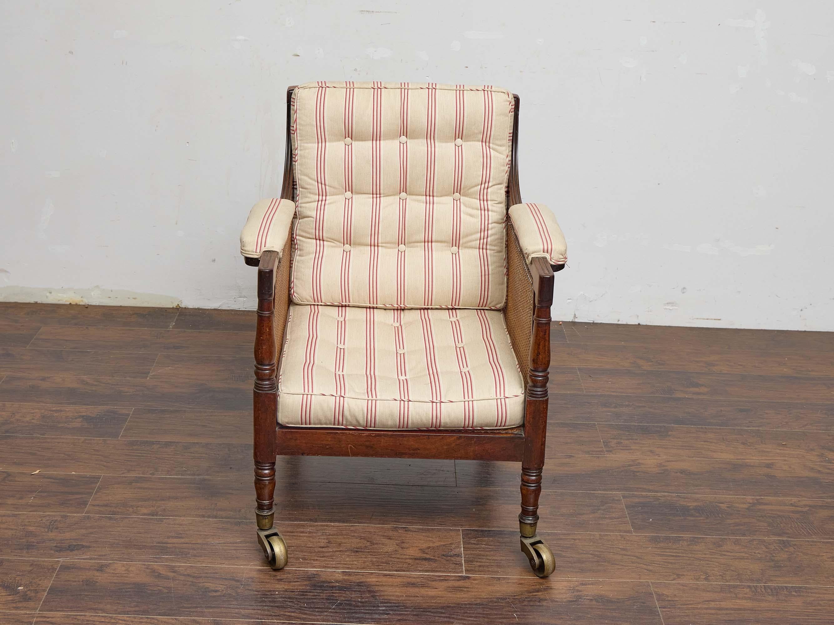 Este sillón de la Regencia inglesa combina la refinada artesanía del siglo XIX con un carácter relajado y habitable. Enmarcada en rica caoba teñida de oscuro, con patas delanteras torneadas y líneas clásicas de la Regencia, la silla presenta paneles