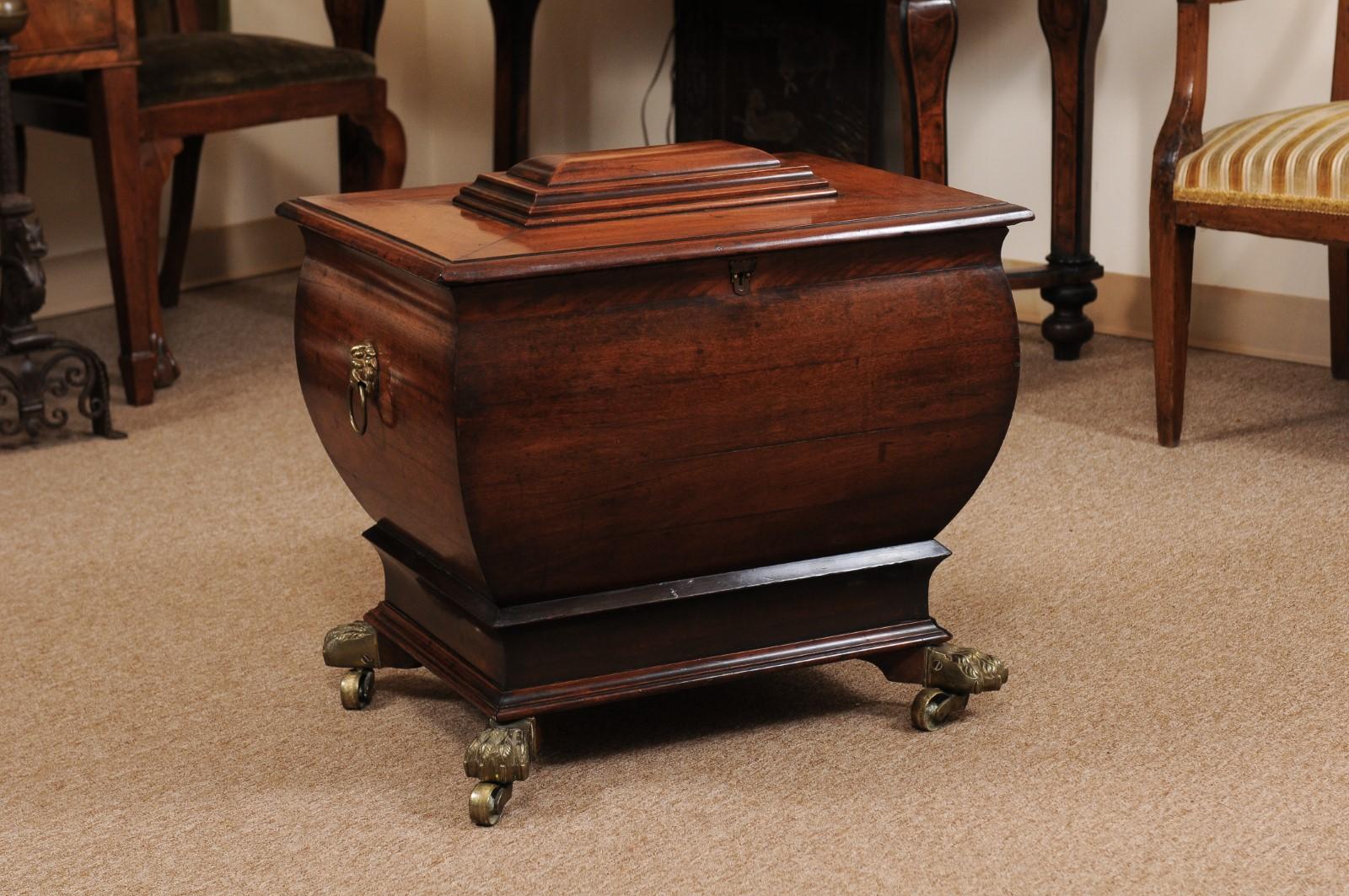 The English Regency mahogany cellarette with convex form, lion head brass pulls and brass paw feet on castors. 

 