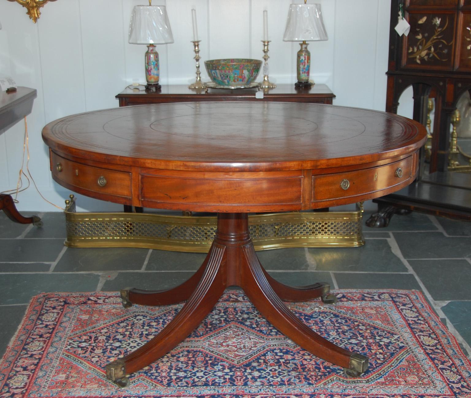 English Regency mahogany drum table with inset full hide hand tooled leather (the leather has been on this table for at least 100 years) . The frieze, with four working drawers and four dummy drawers, is supported by a center turned pedestal with