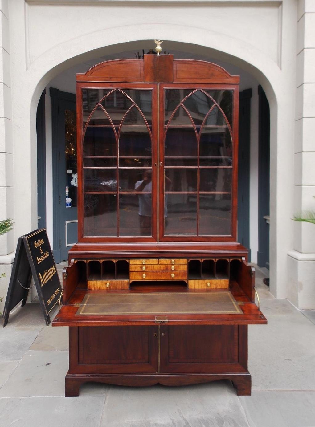 English Regency mahogany secretary with an double arched pediment, centered sphere phoenix finial, upper hinged glass bookcase revealing three interior adjustable shelves, fall front desk with Greek key tooling leather writing surface and satinwood