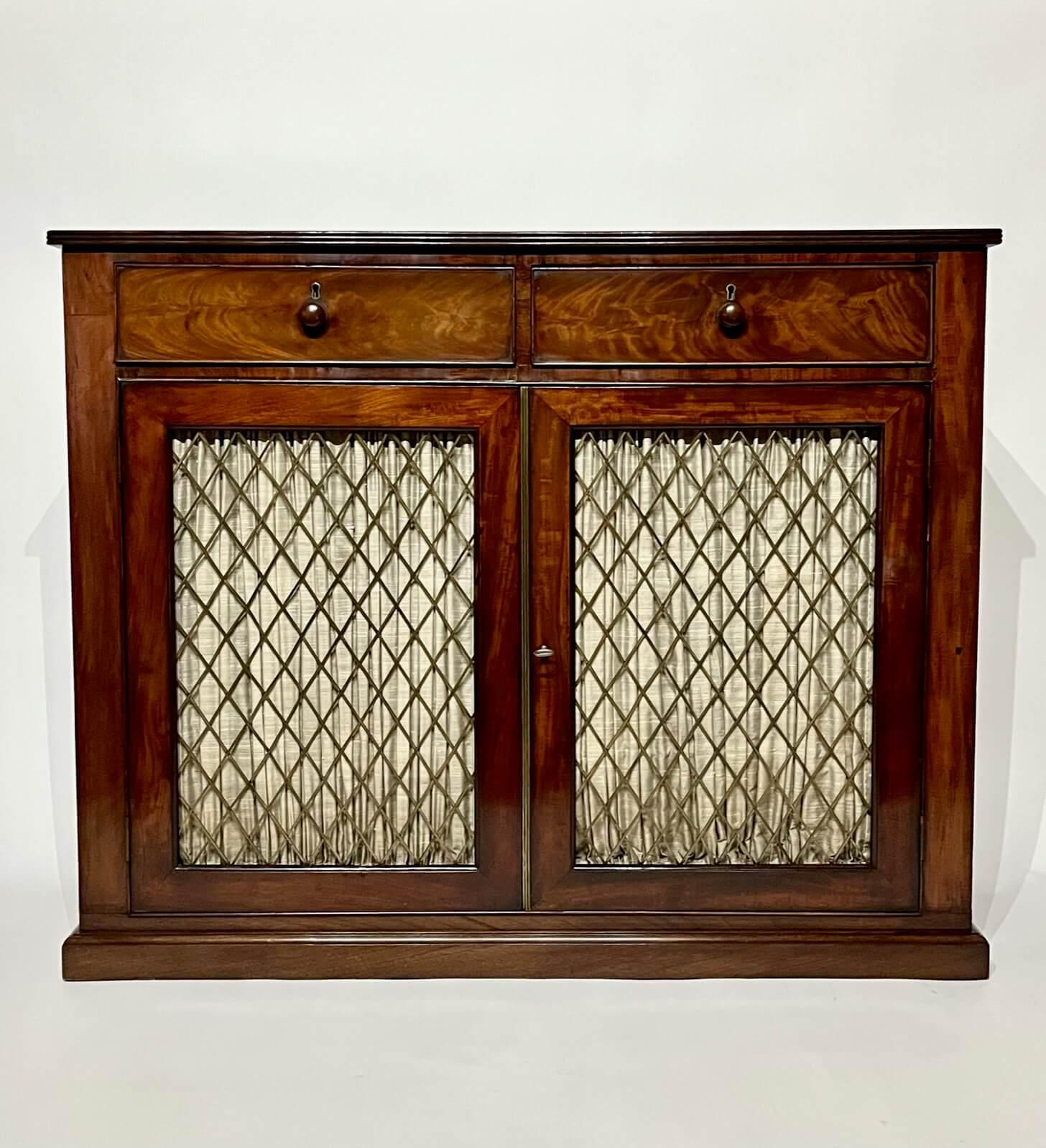 A beautiful circa 1820 English Regency period side cabinet, console cabinet, or low press of narrow rectangular form having exquisitely veneered mahogany case, the top with reeded edge above two locking drawers with original turned knob pulls