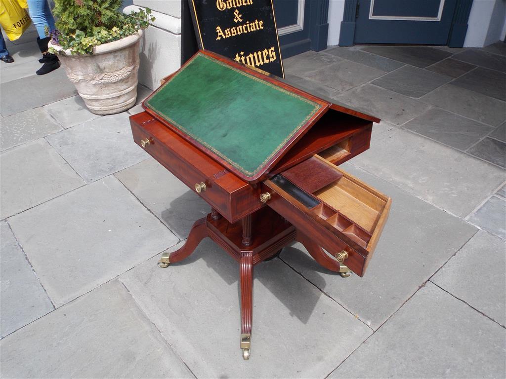 English Regency mahogany partner's reading table with a ratcheted leather top, flanking triangular compartmentalized side drawers with original brasses, supported by four reeded ringed columns on a squared reeded base, and resting on four saber