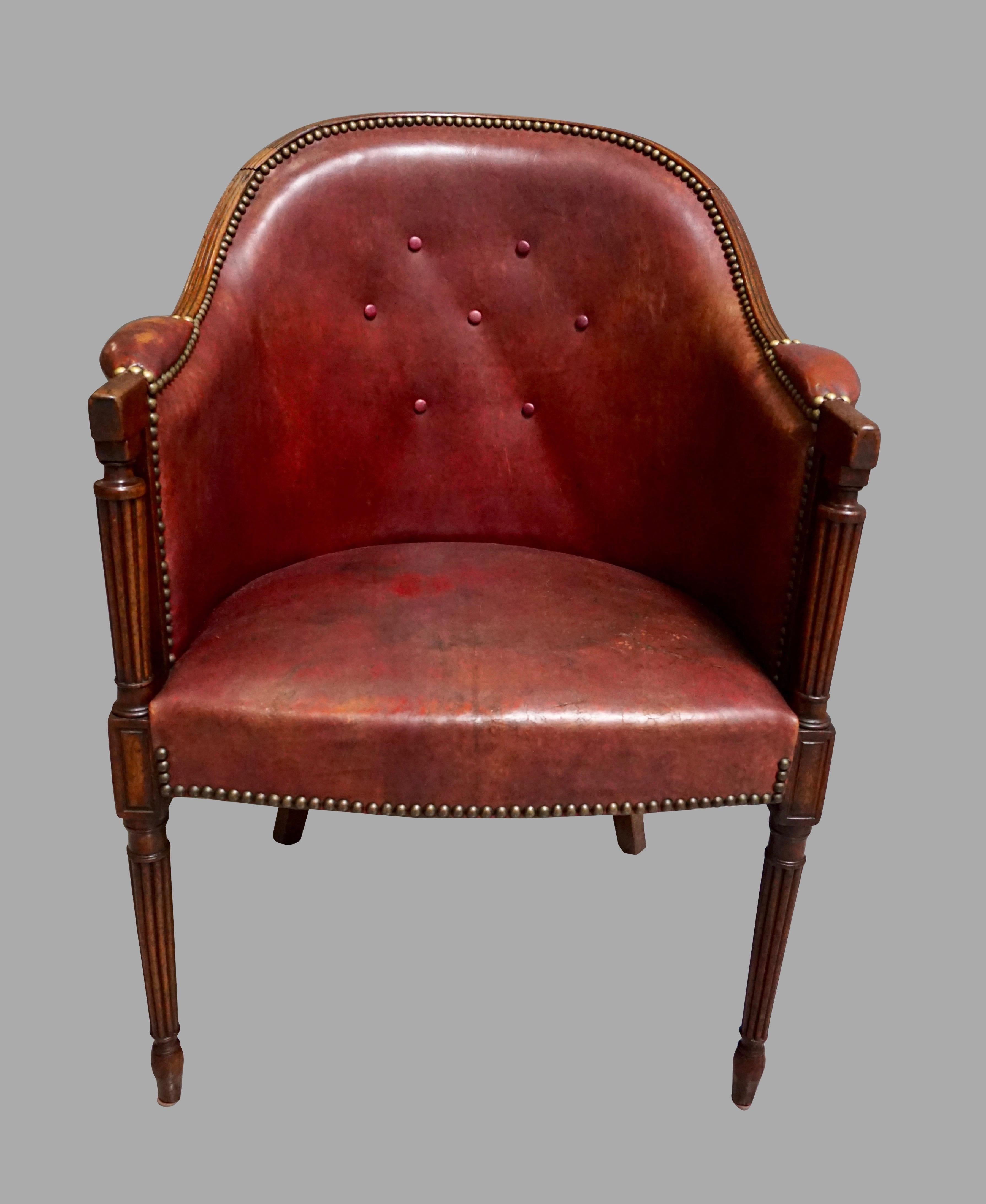 An English Regency mahogany reddish-brown leather upholstered tub chair with nailhead trim, the reeded crest rail above a tufted button back terminating in downswept columnar arms resting on cylindrical reeded legs ending in arrow feet. This chair
