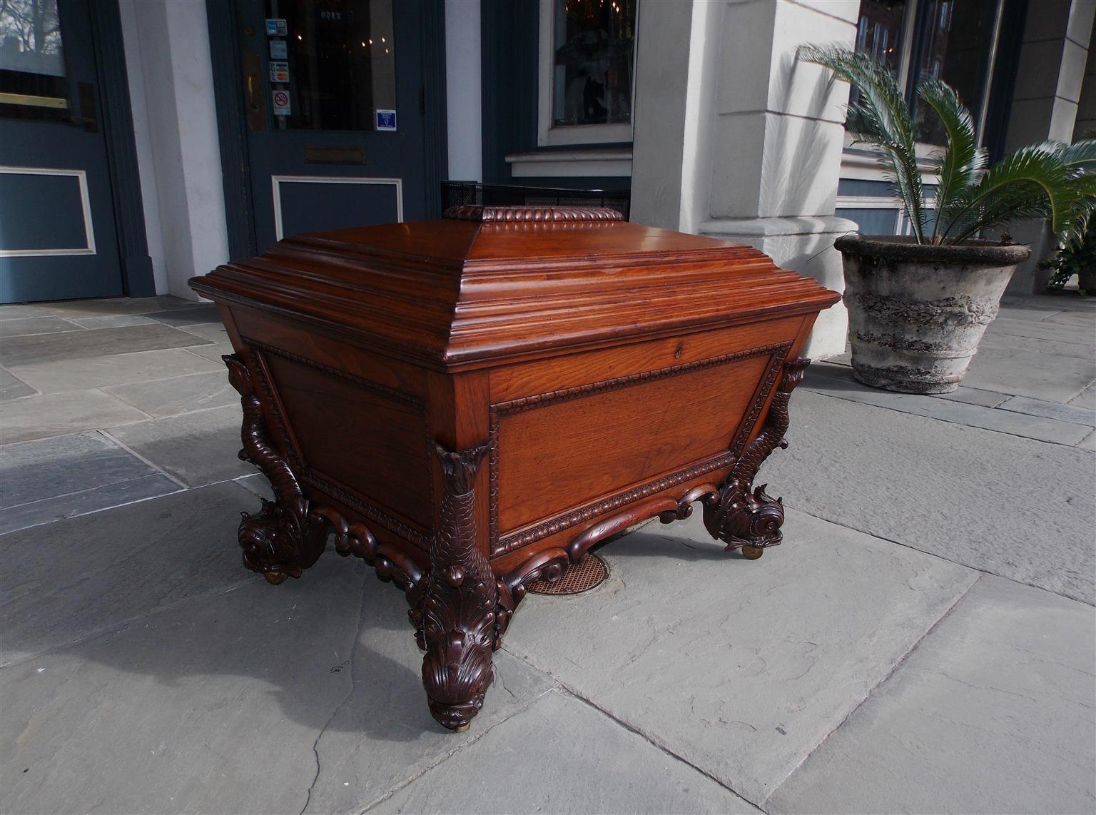 English Regency Mahogany monumental wine cellarette with a gadrooned step back hinged lid, canted gadrooned exterior sides, interior locking mechanism, flanking figural dolphin feet, carved scrolled decorative skirt, and resting on the original