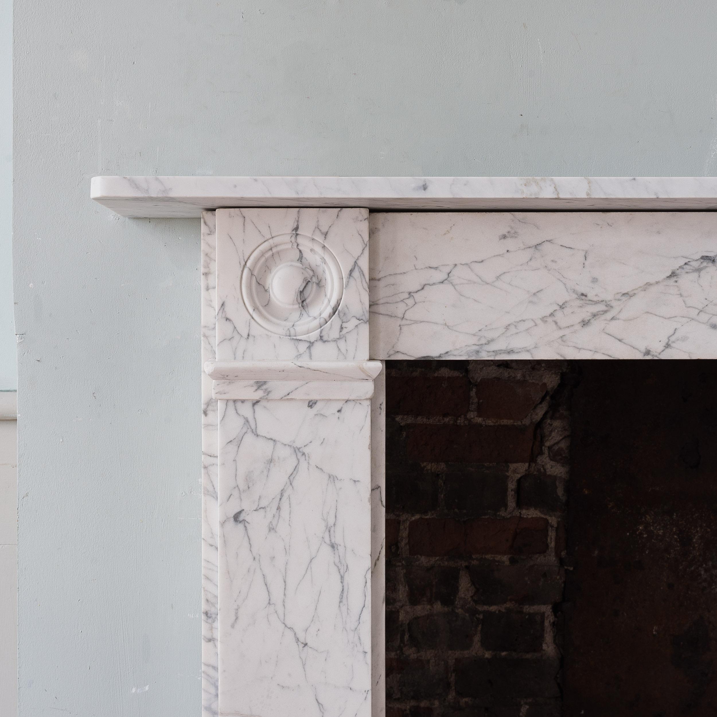 English Regency marble fireplace, of understated design, the rectangular shelf above plain frieze and jambs, with convex roundel corner-blocks, all in well figured Carrara marble with attractive dry surface. Circa 1810.

Opening width 95.5 cm x 92.5