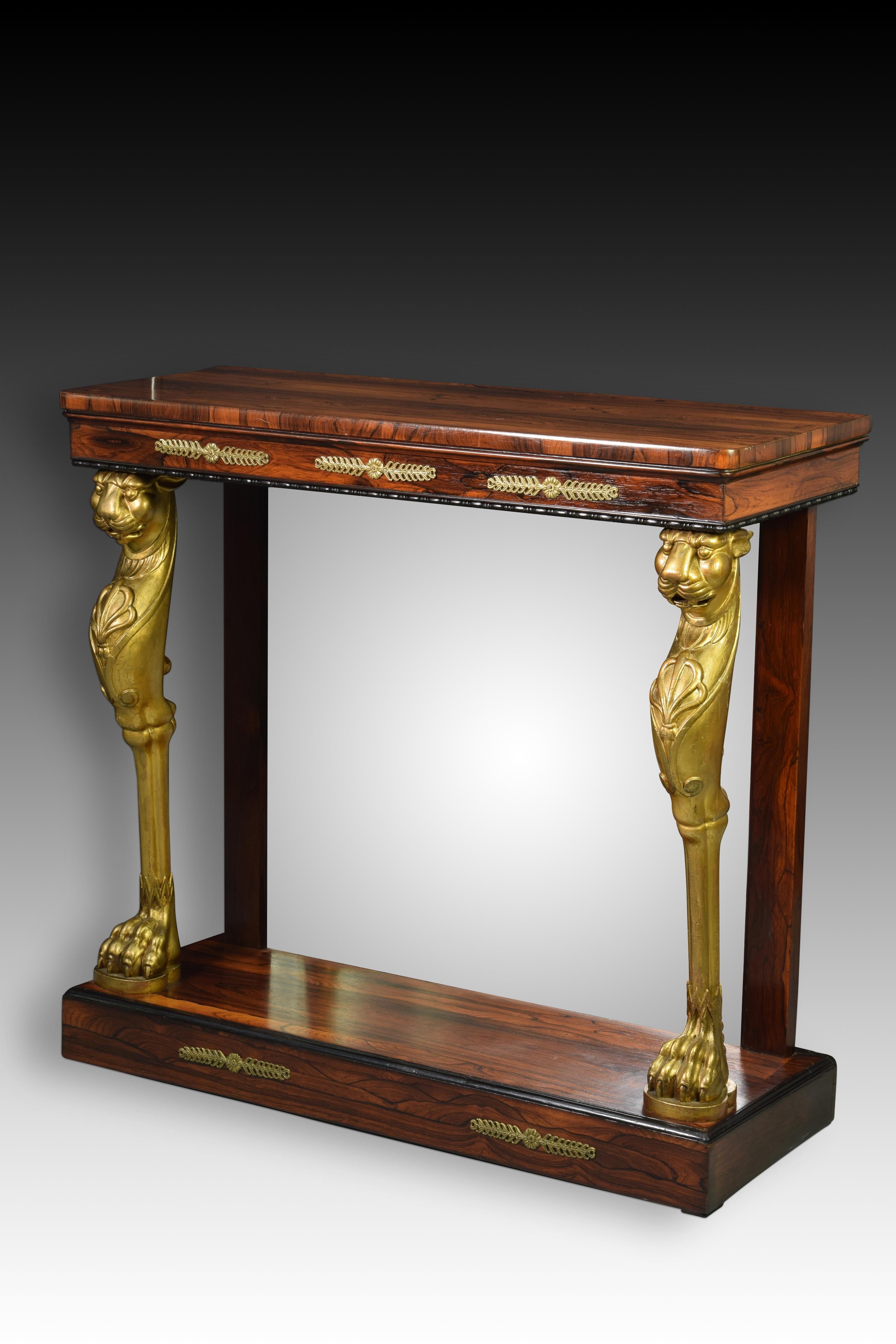 English Regency Console. Rosewood, gilded wood, bronze, mirror. First half of the 19th century. 
Console with a rectangular top with softened edges made of wood that has a waist decorated with gilt bronzes and a band of black architectural