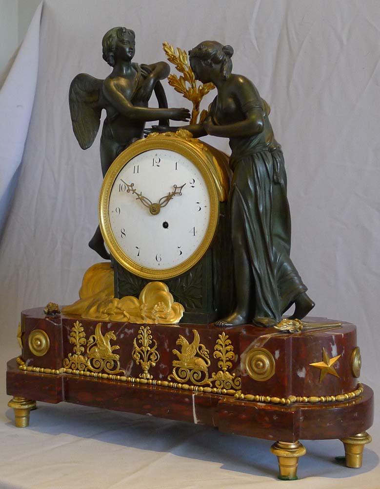 English Regency neo-classical mantel clock of Psyche and Cupid. A fine case of rouge marble, patinated bronze and original ormolu. The superb rouge marble breakfront base with D ends is set upon six two piece ormolu toupee feet. The base is