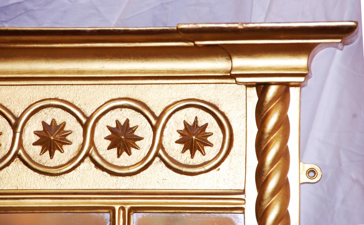 Miroir à trumeau en bois doré de style Régence anglaise de forme tripartite avec des colonnes en torsion d'orge. La frise est une série d'étoiles répétées dans des cercles sous une corniche audacieuse. La corniche, la frise et les colonnes confèrent
