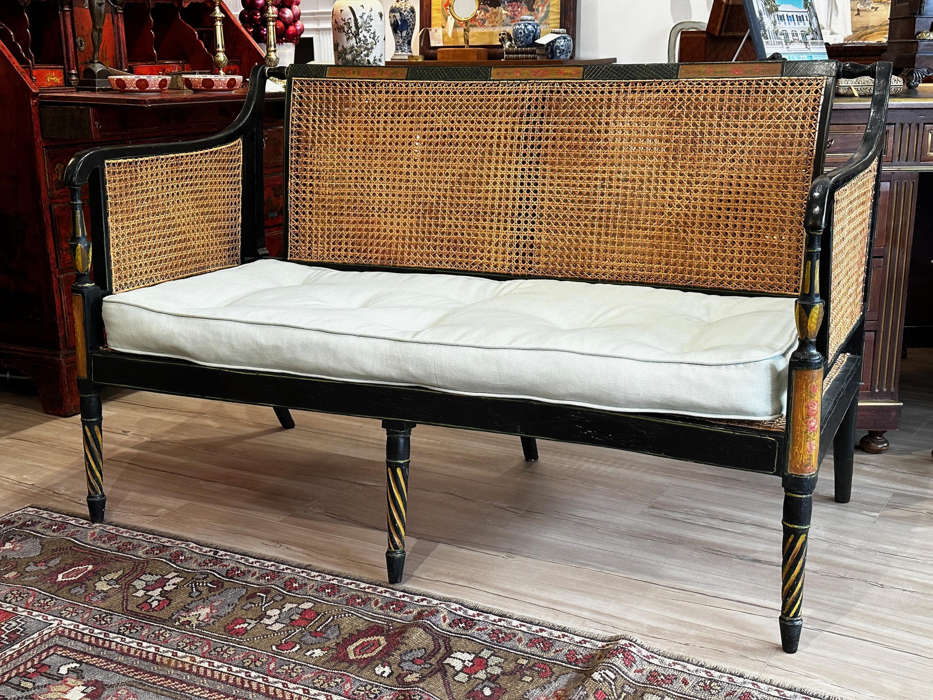 An early 19th century English Regency black lacquer and paint decorated settee or bench, the back, sides, and seat of which are finished with new double-sided hand caning, topped with custom fitted down cushion upholstered in pale blue linen.
