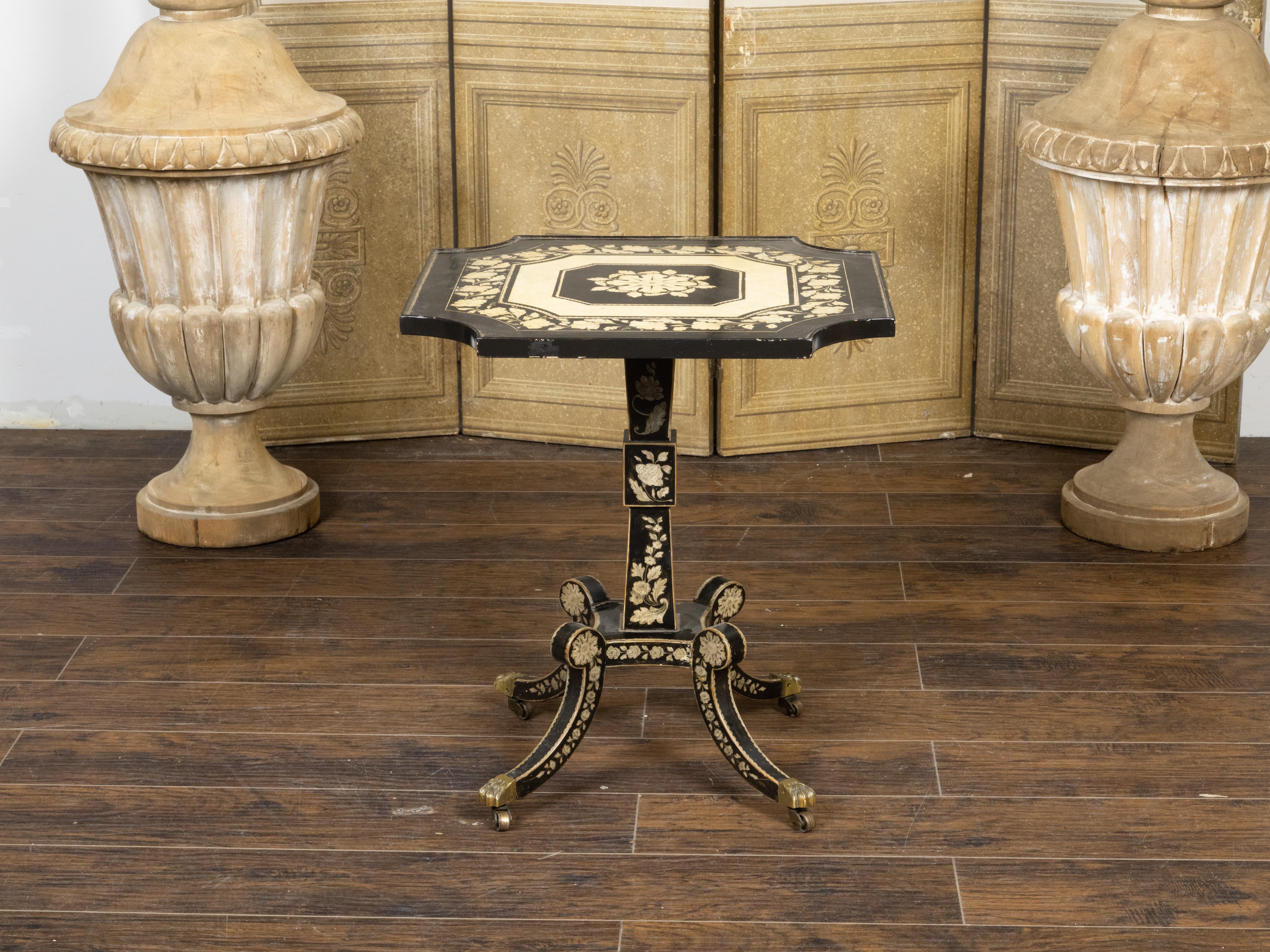 An English Regency penwork occasional table from the 19th century, with square top, in-curving accents, floral décor and quadripod base on casters. Created in England during the Regency period, this occasional table attracts our immediate attention