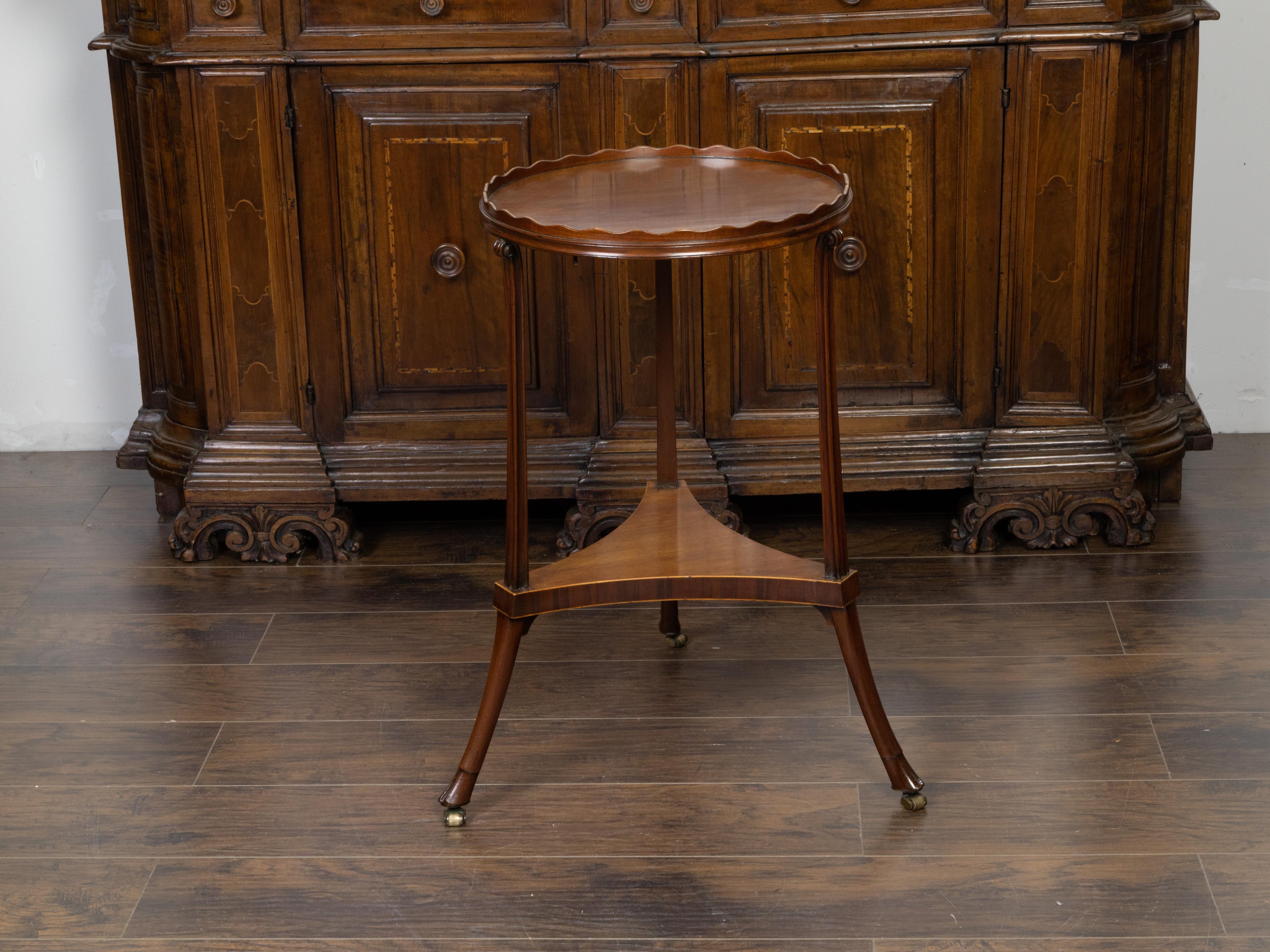 An English Regency period mahogany guéridon table from the early 19th century, with pie crust tray top, tripartite shelf and hoofed feet. Created in England during the first quarter of the 19th century, this mahogany guéridon side table features a