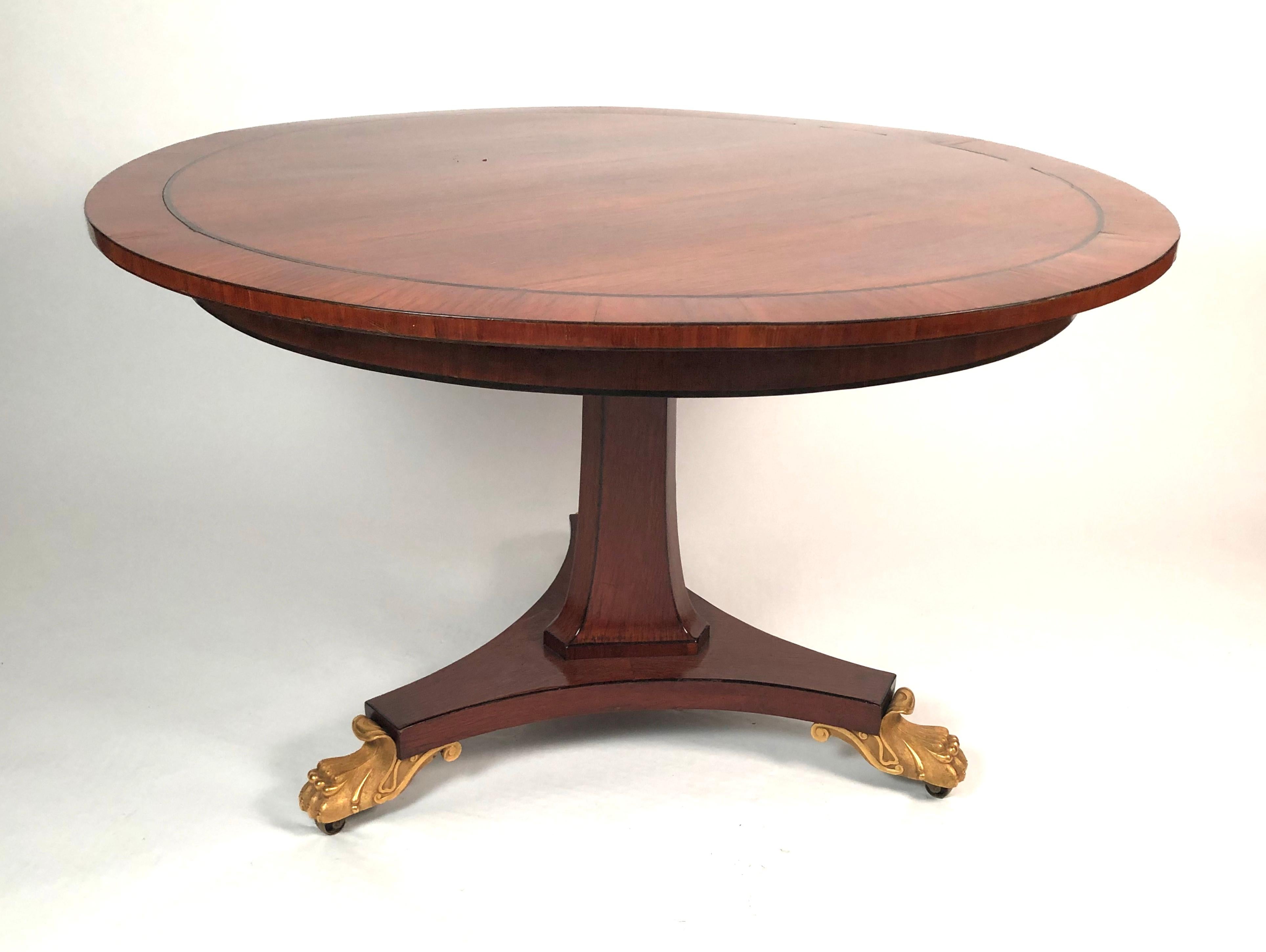 A fine quality English Regency period breakfast or center table in palm wood, the circular top with crossbanding and ebony stringing, supported on a spreading triangular column outlined with ebony stringing, raised on a triangular plinth with