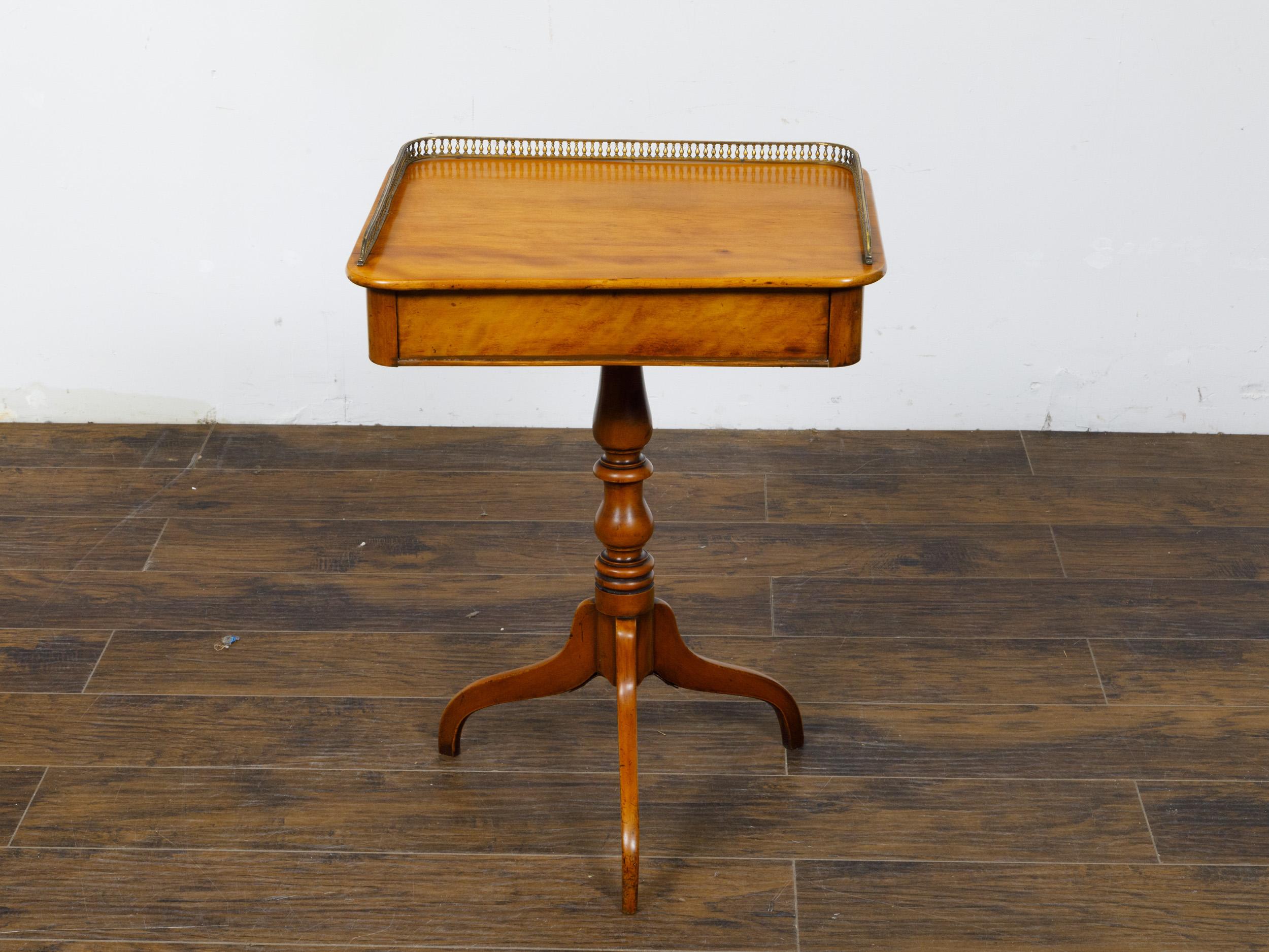 An English Regency period fruitwood guéridon side table from the 19th century with pierced brass three-quarter gallery, turned pedestal and tripod base. This exquisite English Regency period guéridon side table, dating back to the 19th century, is