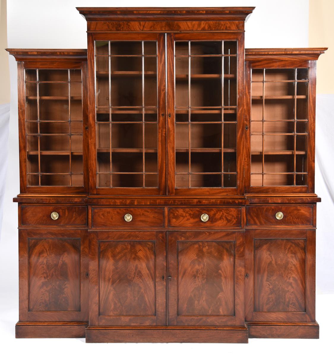 A fine antique English Regency period mahogany breakfront bookcase with stepped up center section. The glazed doors have rectangular panes. The base has four drawers over four paneled doors with highly figured veneered panels. The scale makes it an