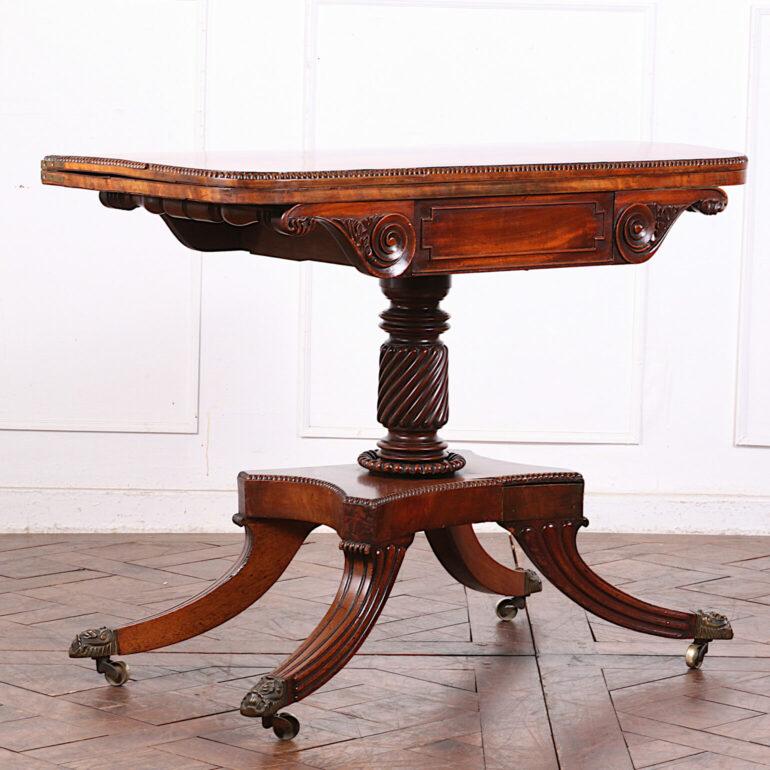 English Regency Period Card Table with a swiveling and opening top to convert from a console to a felt-lined playing surface. Flame mahogany top with banded edge above an elegantly-carved apron, the whole supported buy a carved and spiral-turned