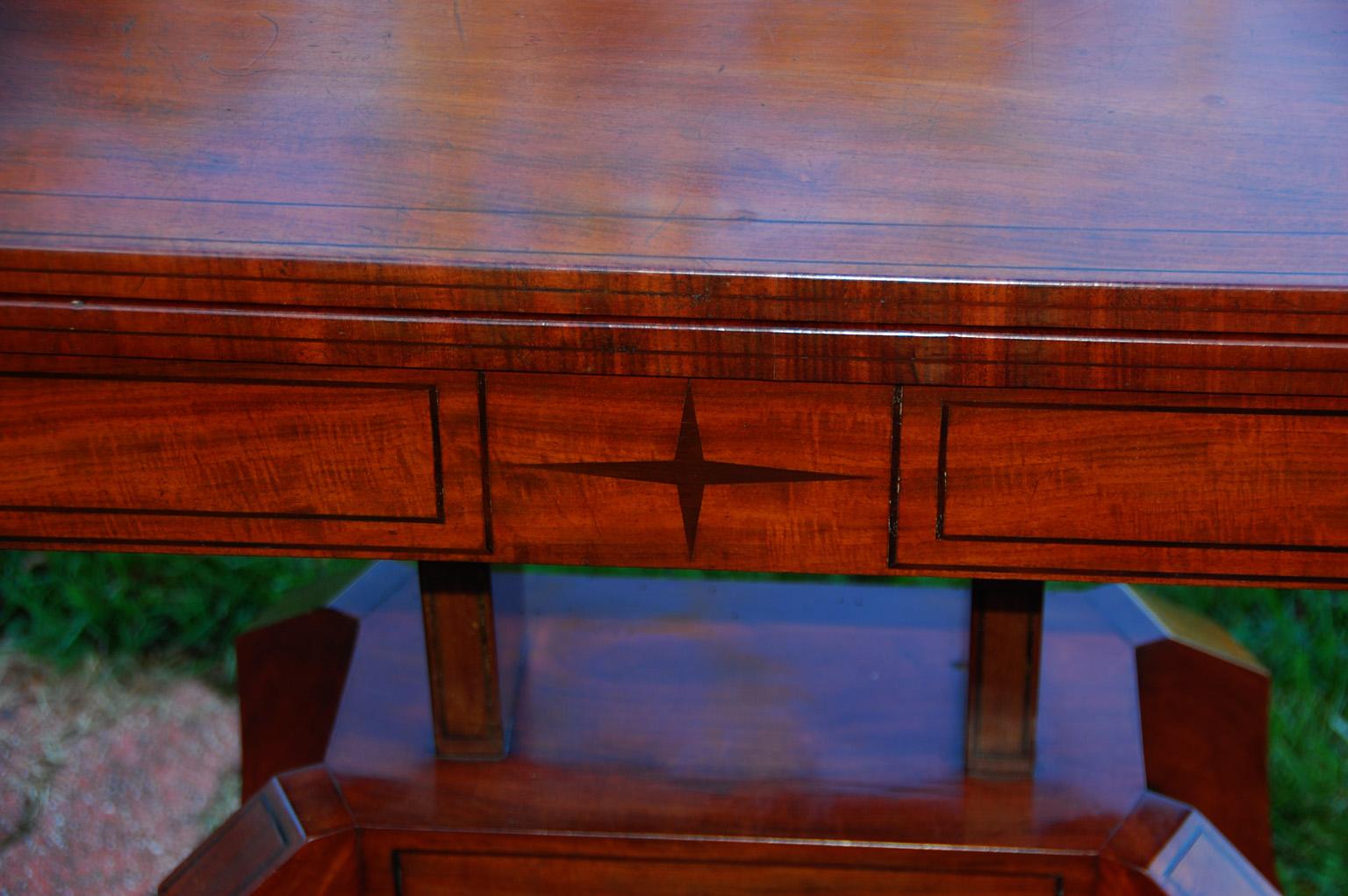 English Regency period mahogany card table with rotating top, cut corners with brass lion masks and extensive ebony stringing and inlay. This handsome table has a pedestal base supported on downswept, ebony inlaid legs. When the top is revolved, a