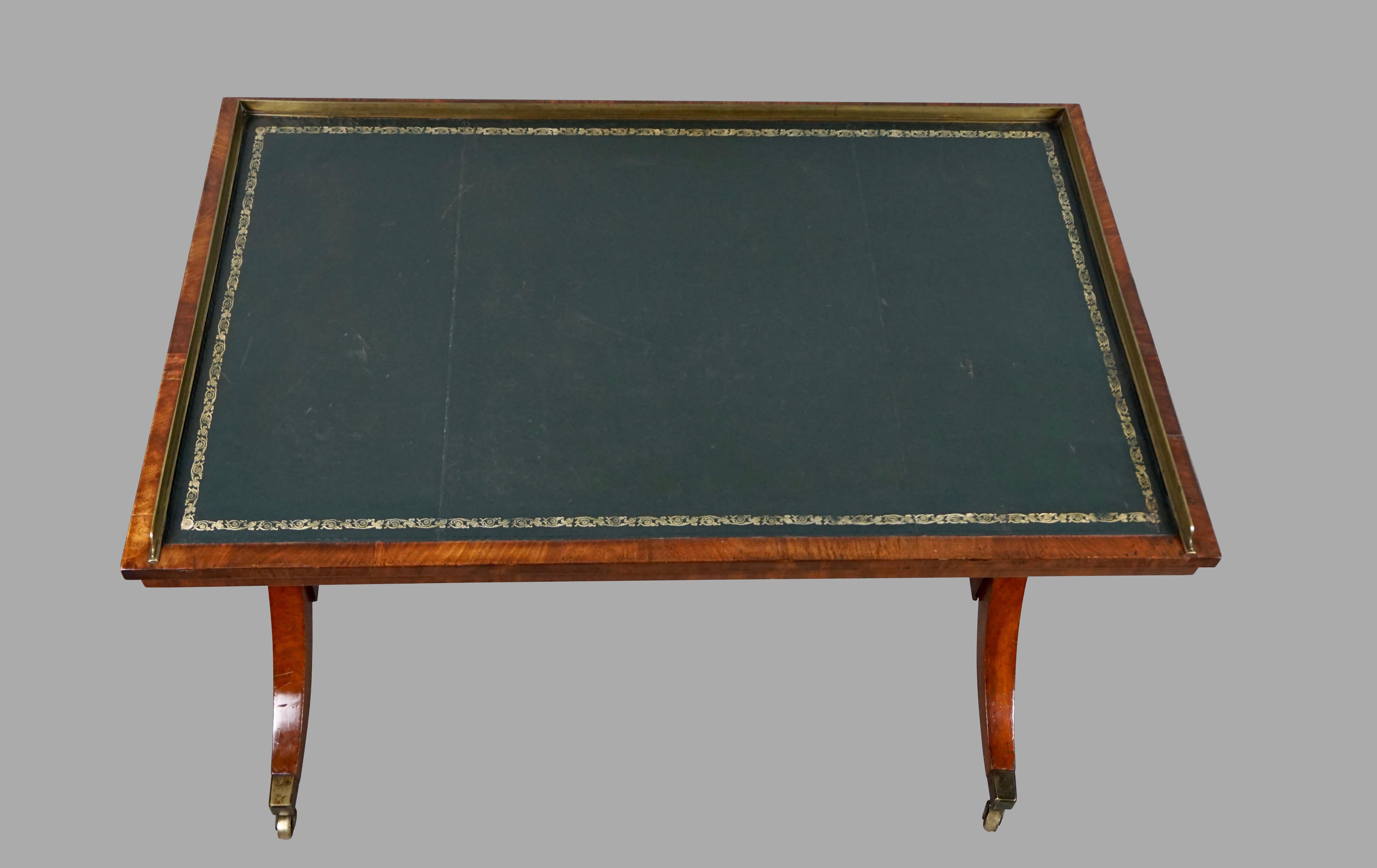 A good quality stylish Regency period mahogany writing table of small size, the gilt-tooled green leather top framed on 3 sides by a brass gallery. The top is supported on standards capped with reeded supports centered by a turned boss terminating