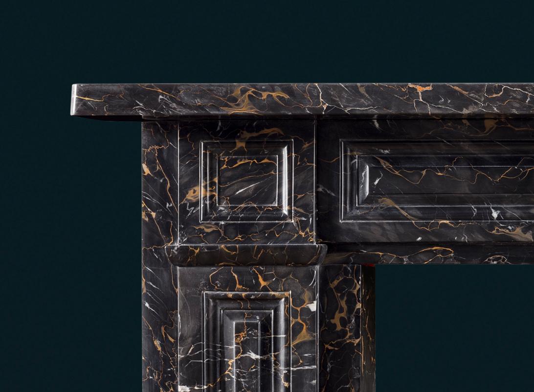 A splendid antique nineteenth-century Regency period Portoro marble fireplace surround, the frieze, corner-blocks and jambs carved with raised and fielded panels. English c.1830.

A smart and assured design which celebrates the elegantly figured and