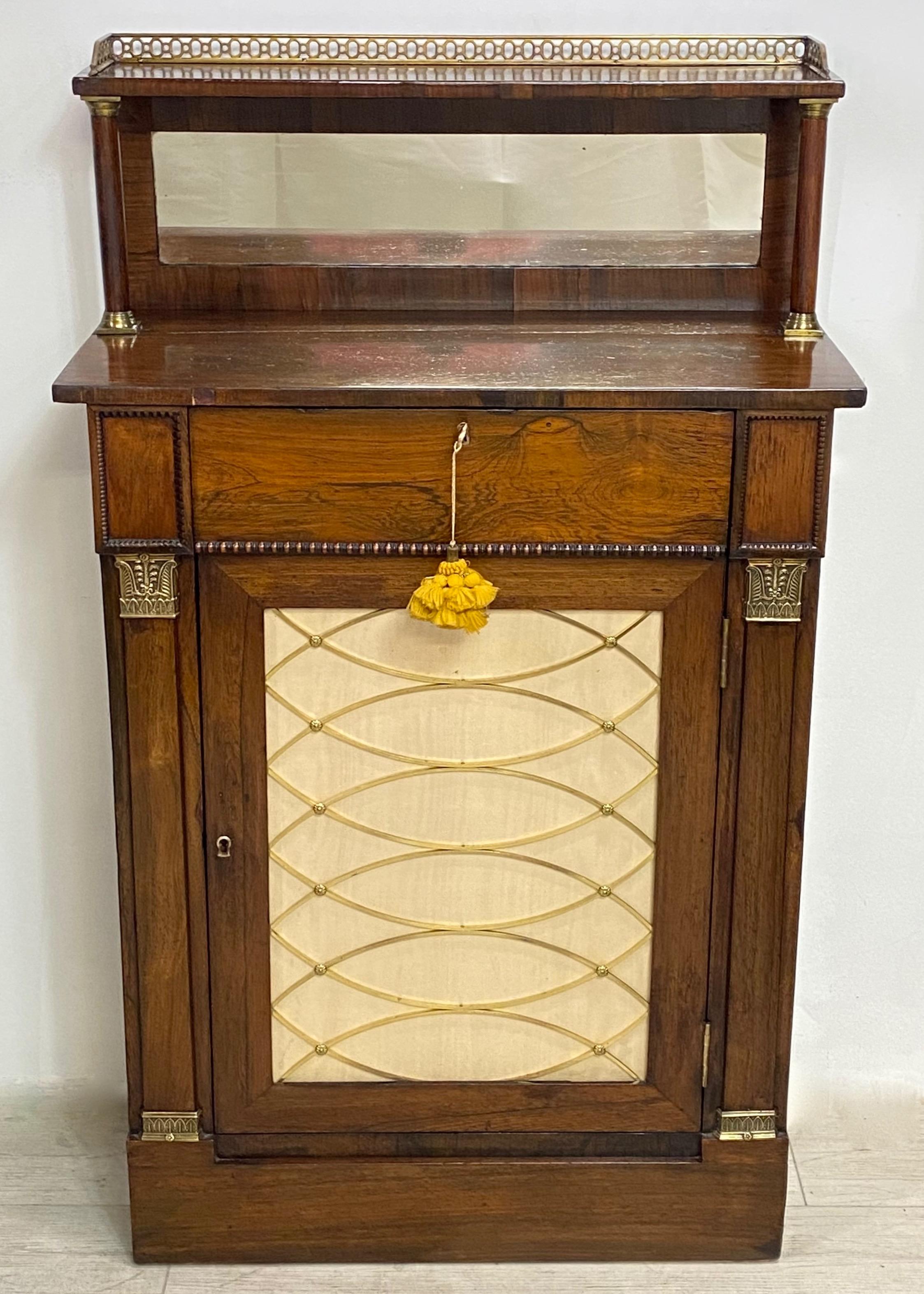 A fine quality diminutive size English Regency rosewood cabinet or chiffonier. Having a pierced gallery top shelf over a center mirror, a single center drawer, original brass grate door front with original silk fabric, and detailed bronze side