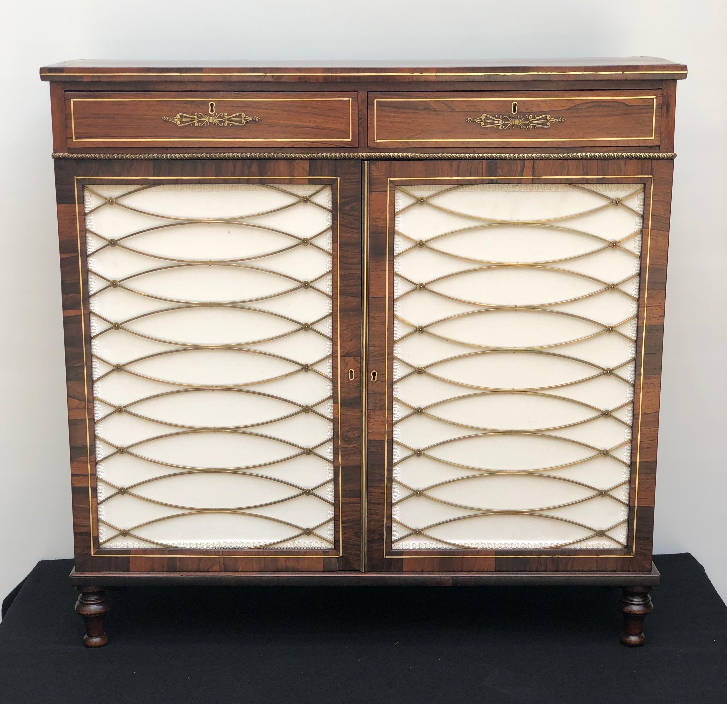 Elegant English Regency rosewood brass mounted, brass inlay credenza / side cabinet having two keyed drawers above two cabinet doors. The two cabinet doors are enhanced with fabric panels and original brass trellis-and-rosette grills. The cupboard