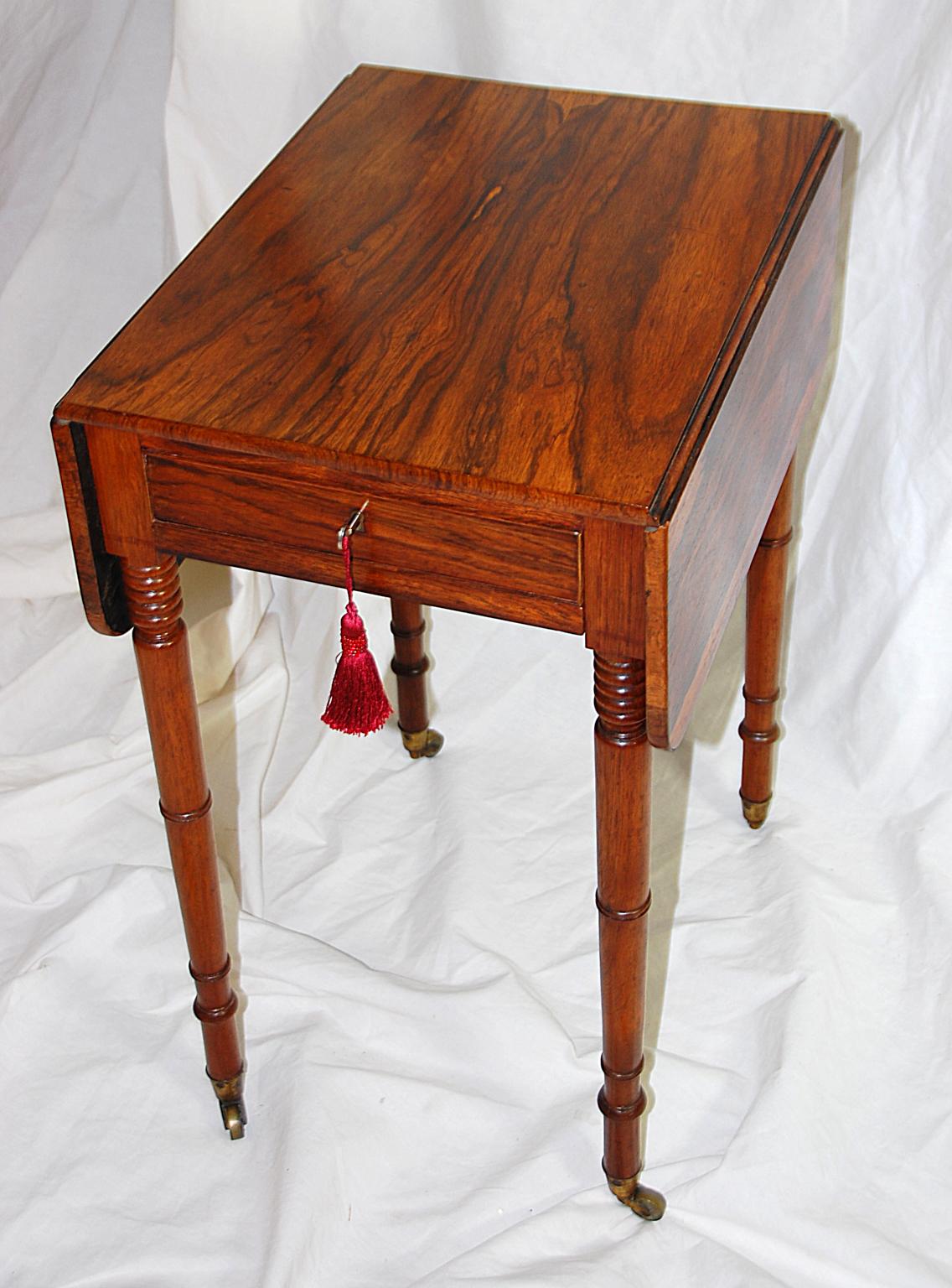 English Regency period rosewood one drawer drop-leaf side table with delicate turned, tapered legs. The sewing basket that originally hung below the drawer has been removed and replaced with a pullout / pull-out leathered slide; the original framing