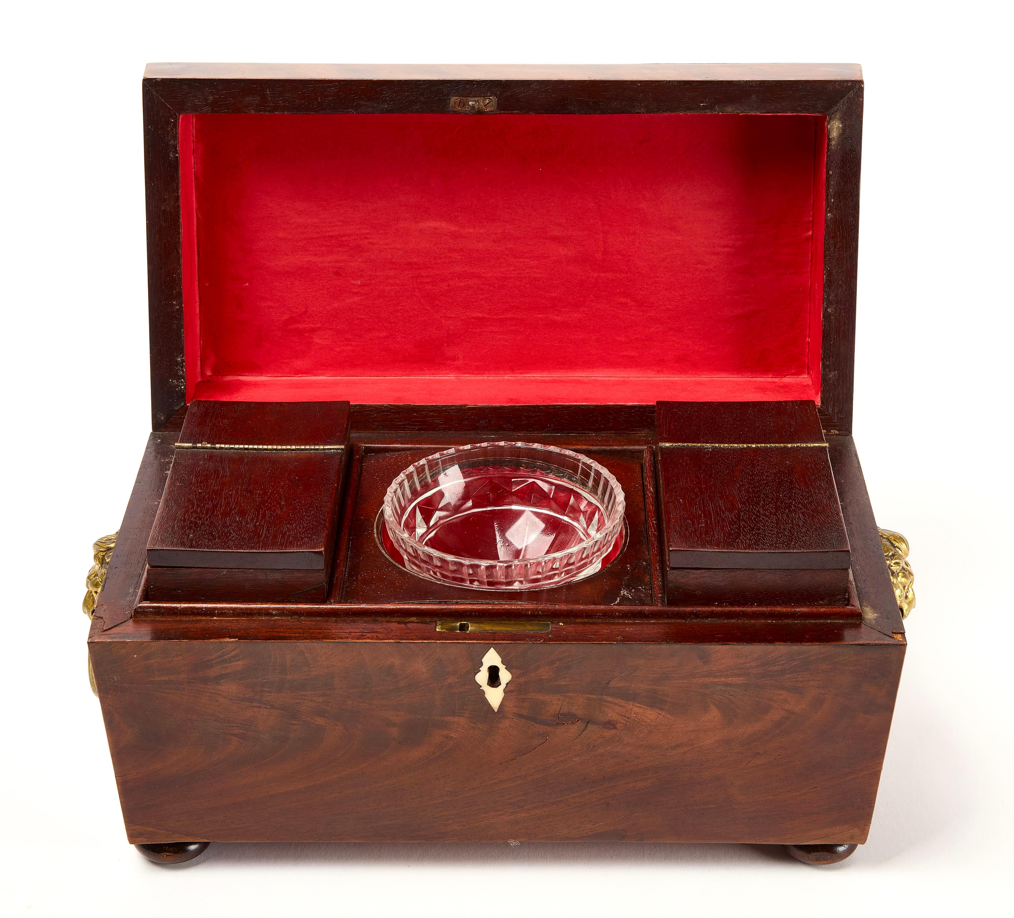 Boîte à thé en acajou de style Régence anglaise. Le Tea Caddy se présente sous la forme d'un sarcophage dont le couvercle à charnière dissimule un intérieur en trois parties. L'intérieur comporte un bol à mélanger en verre au centre, flanqué de