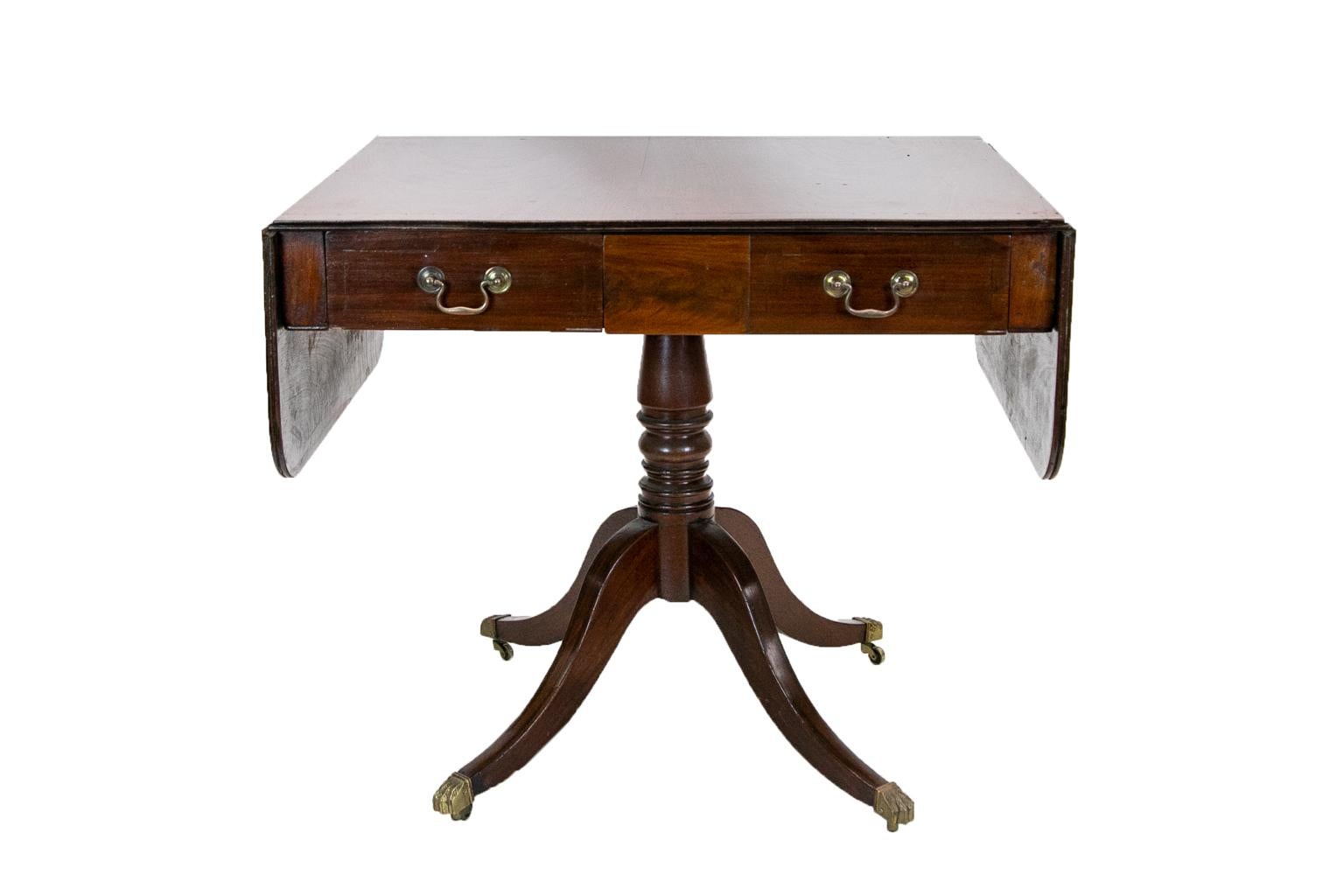 The top of this sofa table has an inlaid band. The drop leaves are supported by double extending butterfly supports. The base has a turned stem and is supported by four inlaid sweeping legs that terminate in brass hairy paw castors. It is 56.75''