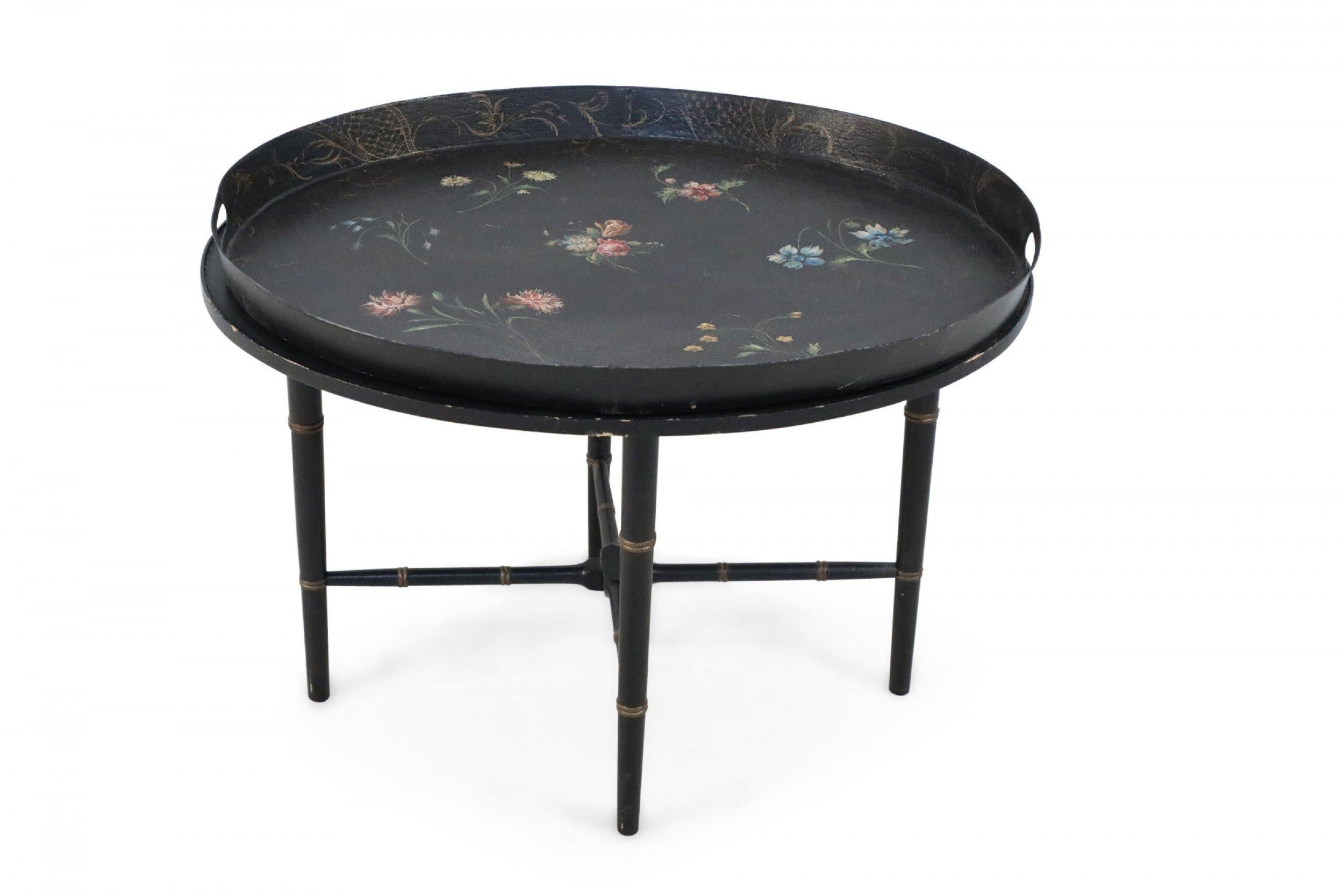 English Regency-style tray top coffee table in black, topped with an oval, removable tray painted with spaced pink and blue floral bouquets, sitting atop gold-accented ebonized faux bamboo metal legs that are connected with an x-shaped