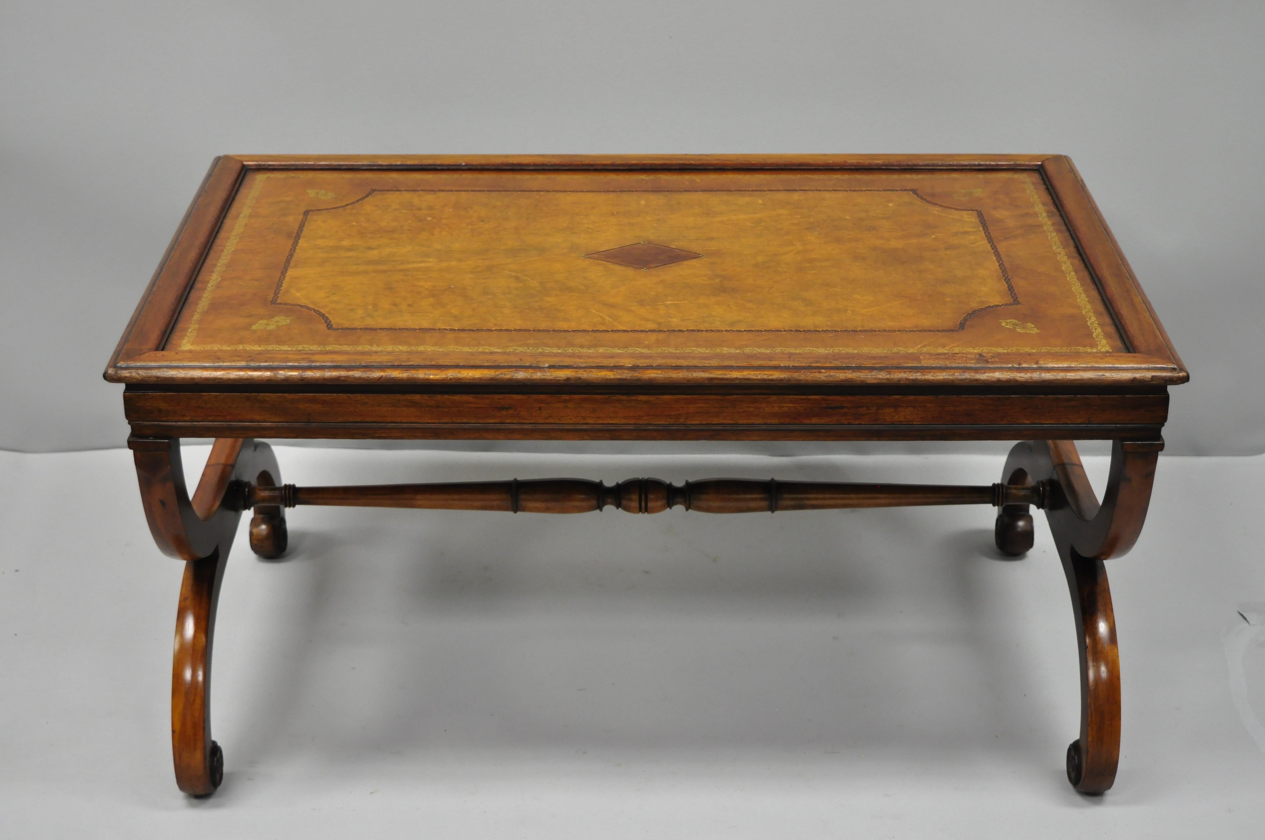 Vintage English regency style tooled leather top curule coffee table. Item features a brown tooled leather top, curule form legs, stretcher base, solid wood construction, beautiful wood grain, great style and form, circa early to mid-20th century.
