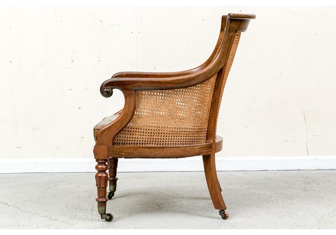 Bergère de style Regency avec assise capitonnée vert olive, pieds avant tournés avec capuchons et roulettes en laiton et pieds arrière évasés avec roulettes en laiton. La bergère présente des côtés et un dossier cannelés, des accoudoirs en C, une