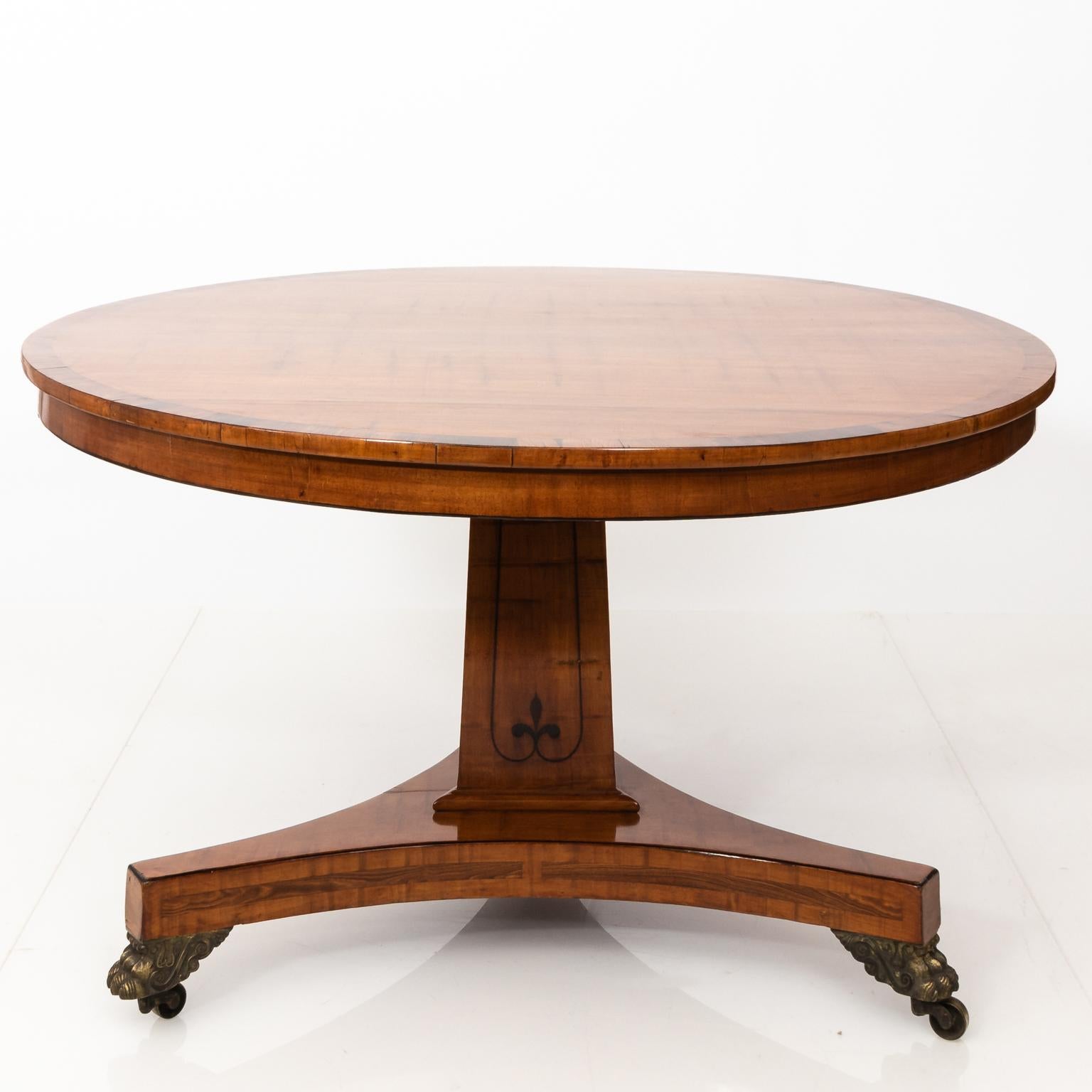 English Regency style center table in satinwood with rosewood banding on a pedestal base with brass lion's paw castors, circa 1900.
 