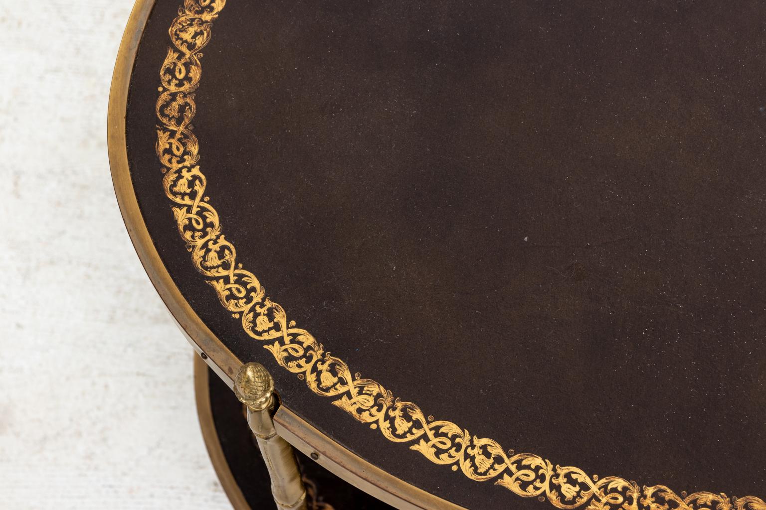 English Regency style two-tier oval cocktail table with embossed leather tops and brass faux bamboo legs, circa 1980s. The leather top is decorated with embossed foliage trim. Please note of wear consistent with age.