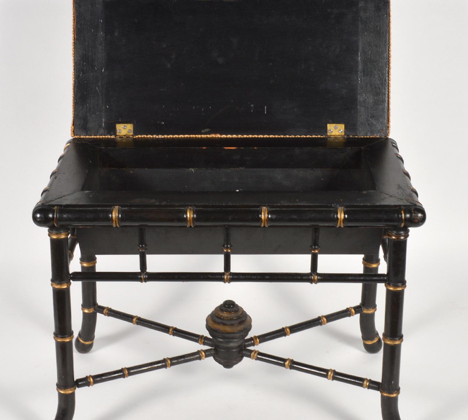 This elegant Regency style bench features an ebonized and gilt accented faux bamboo frame with four splayed legs united by a low x-stretcher centering a carved and turned ornament, 19th century. The upholstered seat opens up to an interior storage