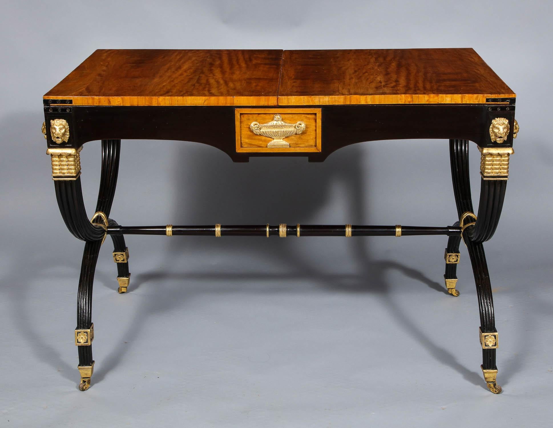Fine satinwood, gilt and ebonized extending table in the manner of John McClean, circa 1890, having well figured top over ebonized shaped apron with gilt lion and urn mounts, standing on ribbed curule legs with gilt bands and standing on brass