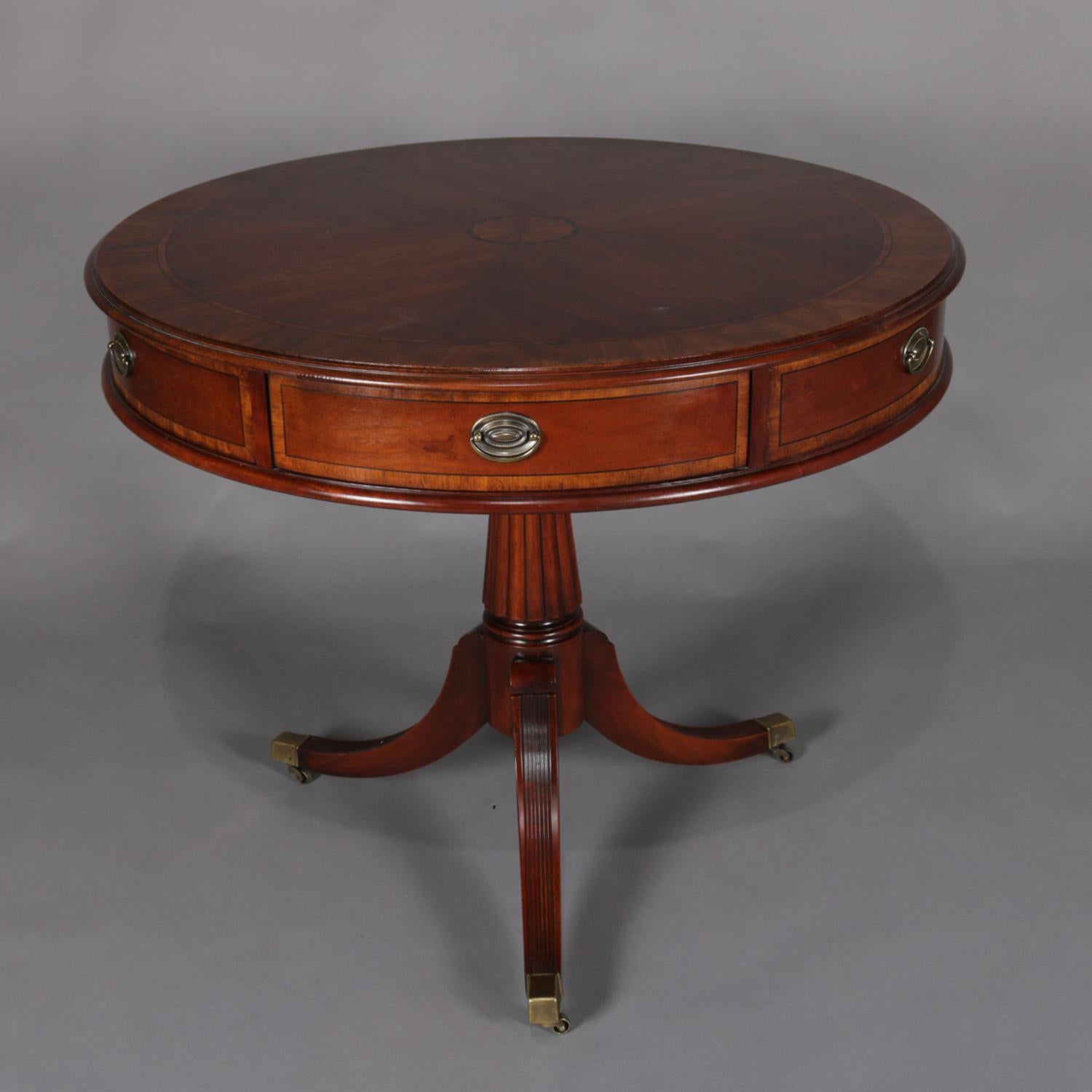 An English Regency style center table by Lexington in the Palmer Home line featuring circular drum form with bookmatched top having central inlaid patera medallion over skirt with six drawers, raised on reeded pedestal base with Sheraton Duncan