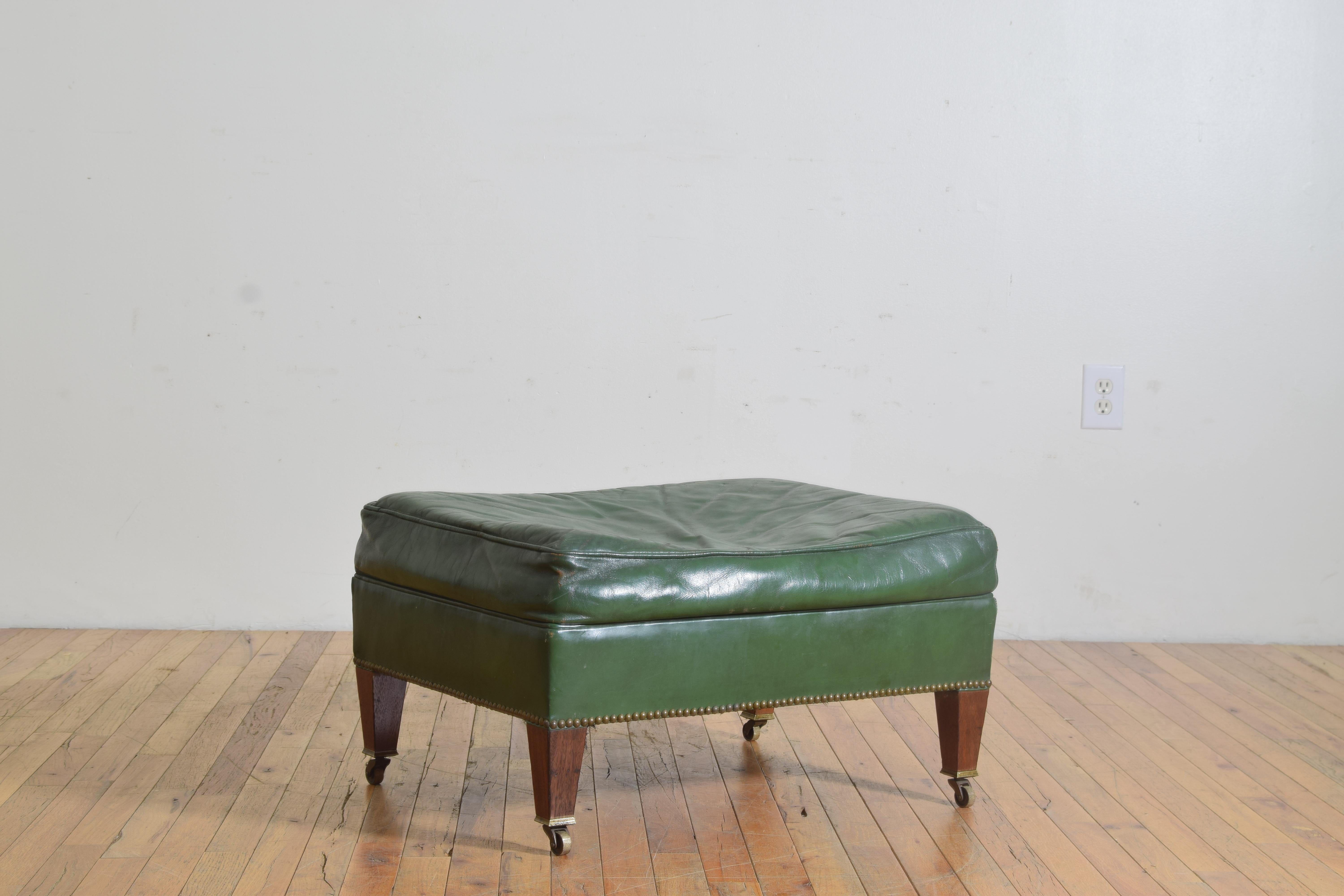 Having a rectangular down filled cushion top above a conforming frame, both upholstered in original green leather, raised on square tapering legs with original wheel casters
