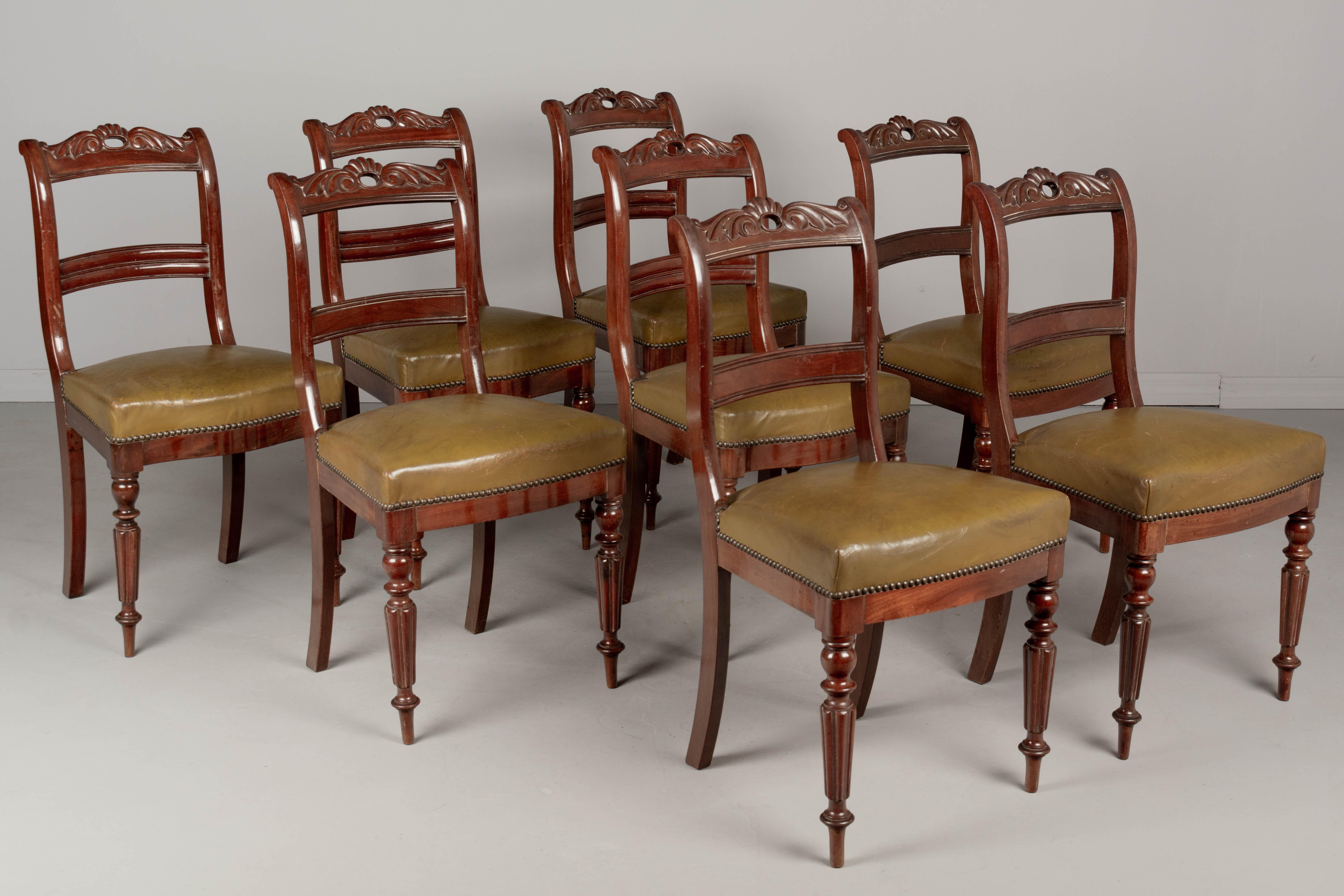 A set of eight English Regency style mahogany dining chairs, nicely detailed with turned fluted front legs and curved back with carved decoration. Sturdy and well constructed. Original leather upholstery with brass nail head trim. Leather with nice