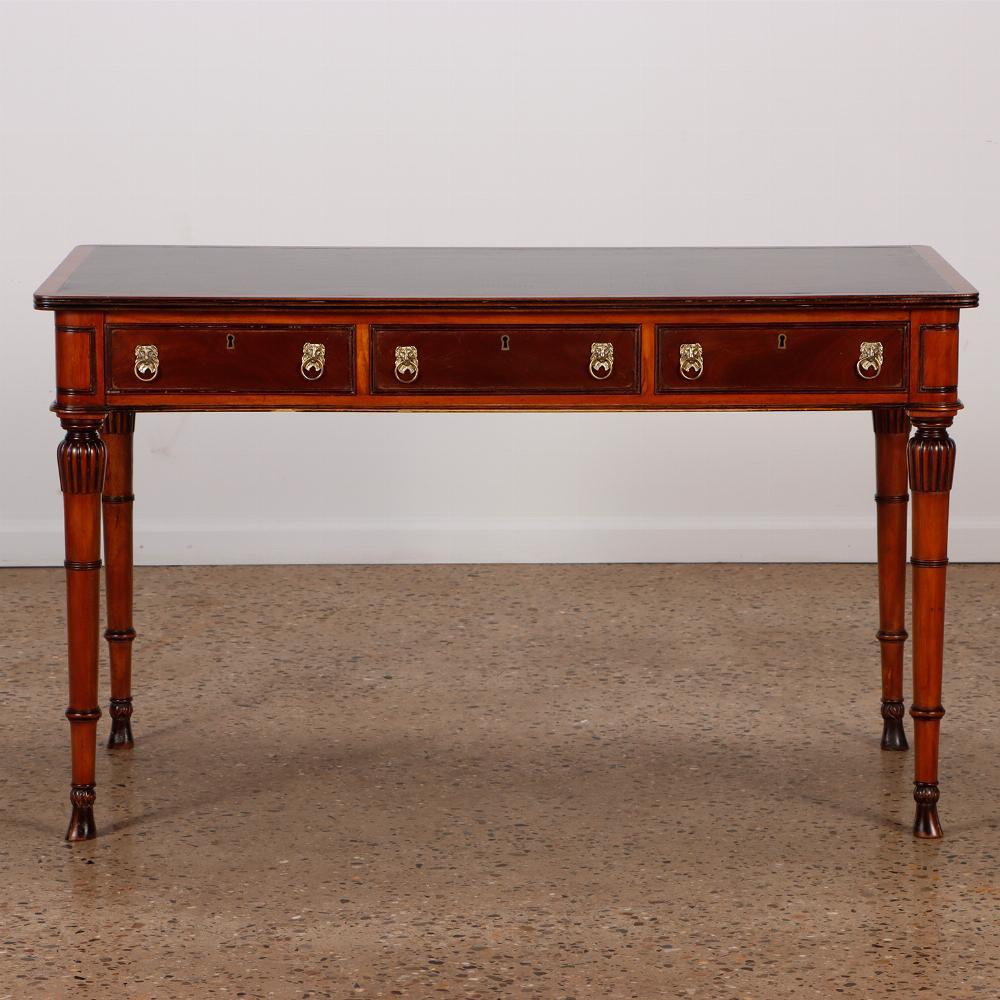 English Regency style mahogany leather top writing desk C 1950 having black leather inset top, above three drawers with lion drop drawer ring pulls, supported by turned, fluted and ring carved legs, and overall ebonized details.