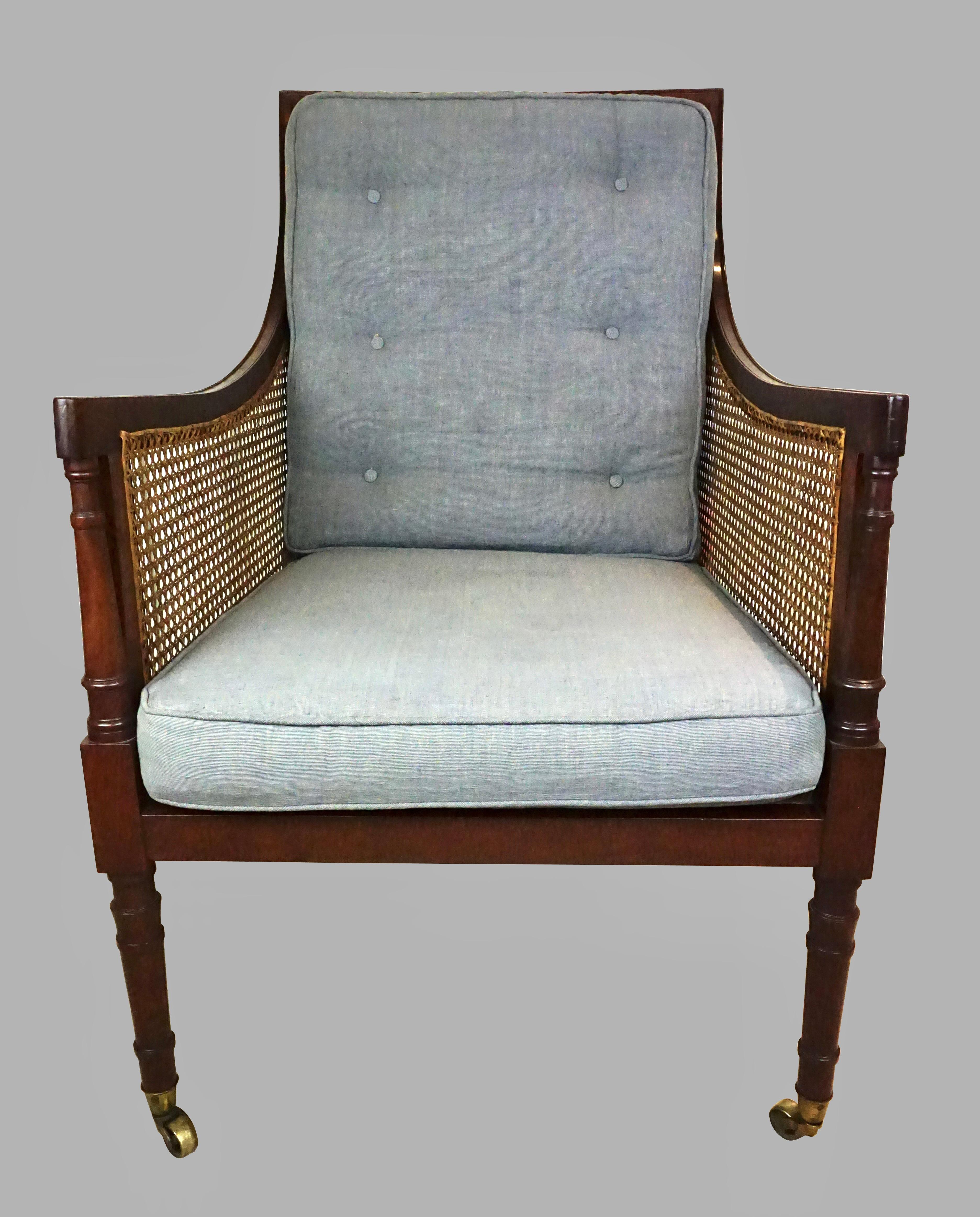A large scale English Regency style mahogany library bergere armchair, caned on the front, sides and back, with removable bluish gray linen seat and back cushions, raised on turned front legs terminating in brass casters. This chair sits very well